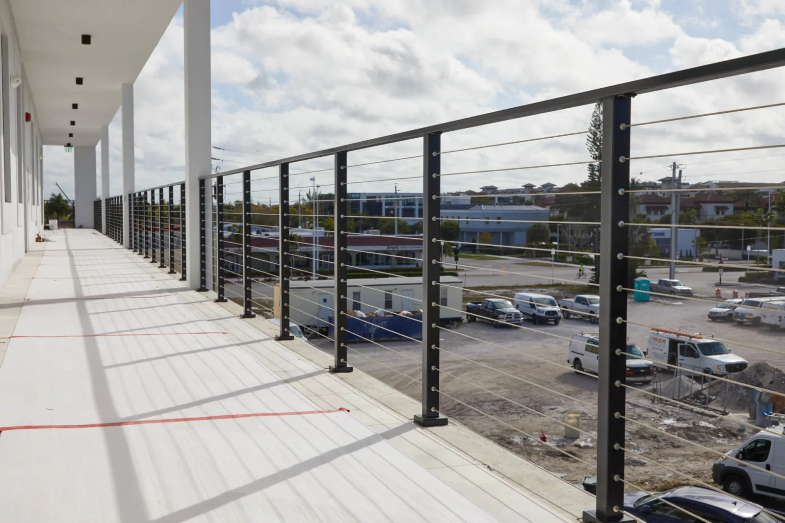 Long upper walkway lined with black cable railing above a parking area