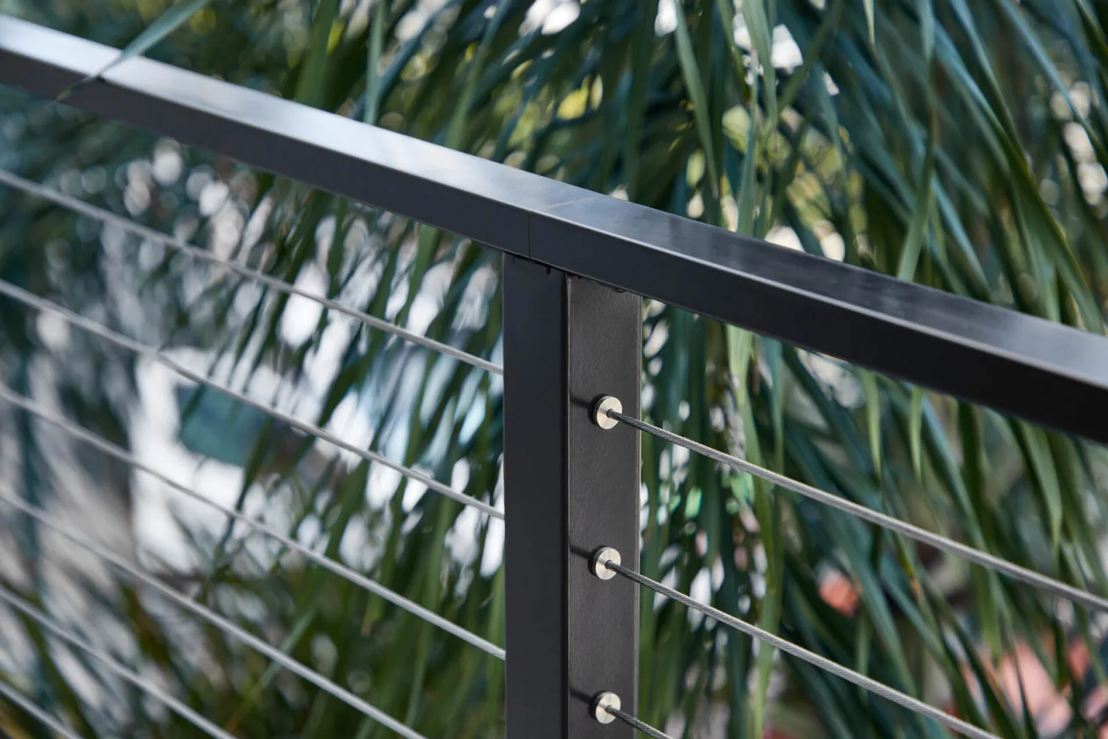 Close view of a black post and flat top rail against palm fronds