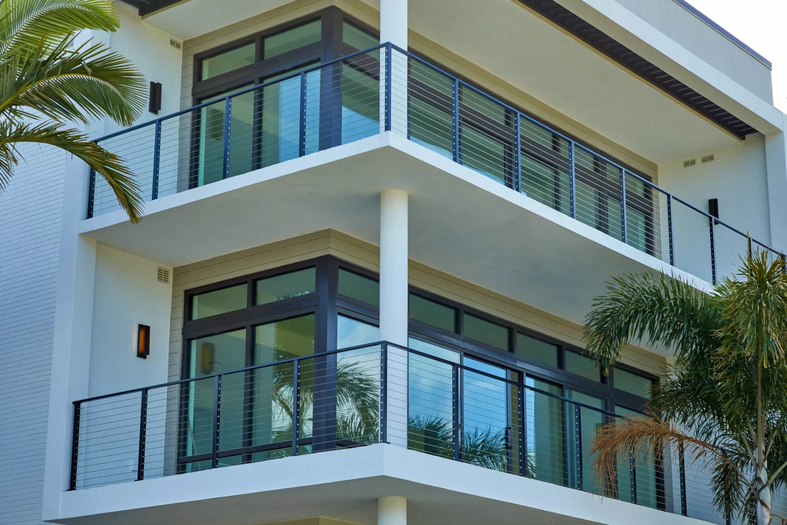Two stacked balconies with black posts and cable infill beside dark-framed windows