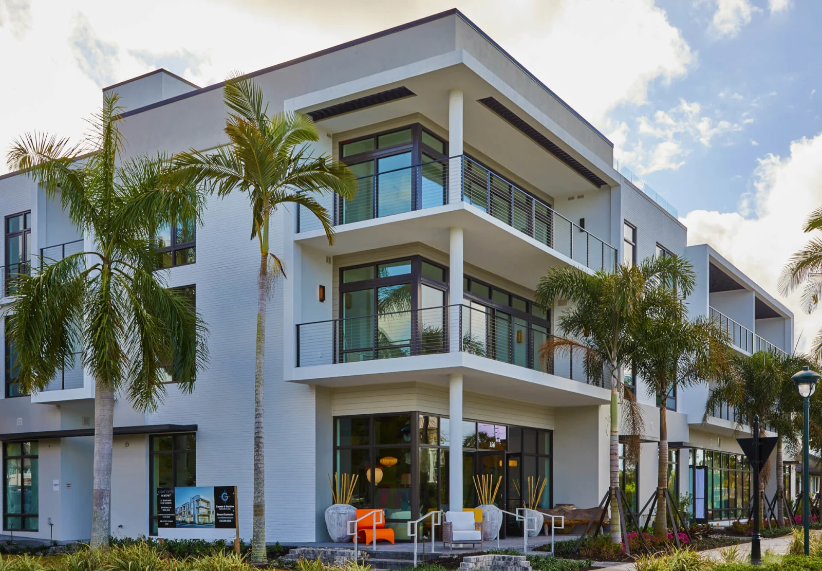 Palm trees fronting a white three-story building with slim black balcony railings