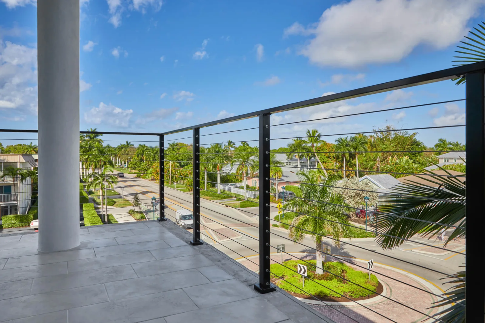 Corner balcony with tile floor and cable railing over a palm-filled neighborhood
