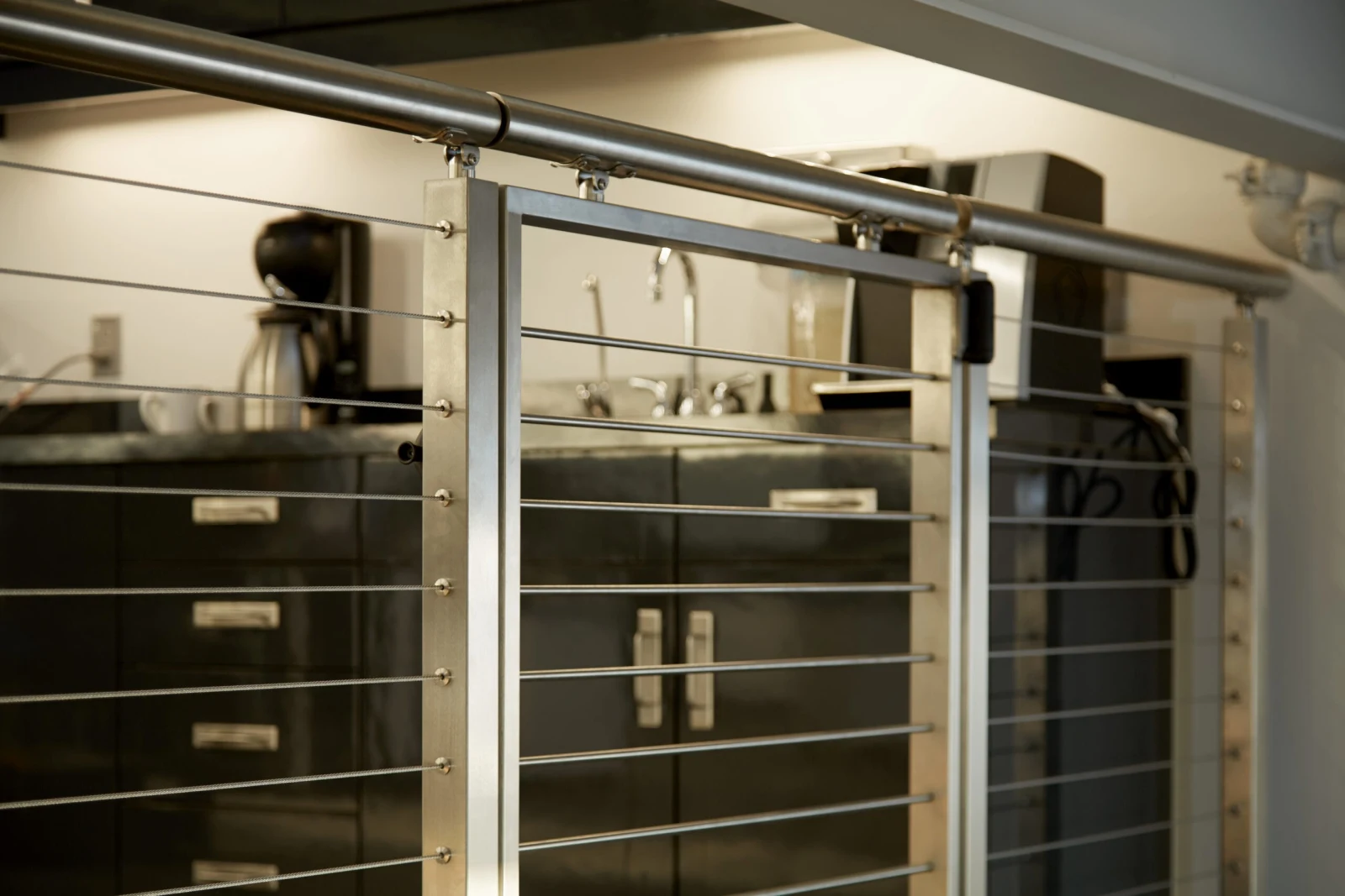 Stainless posts and cables under a round metal handrail screening a laboratory workbench