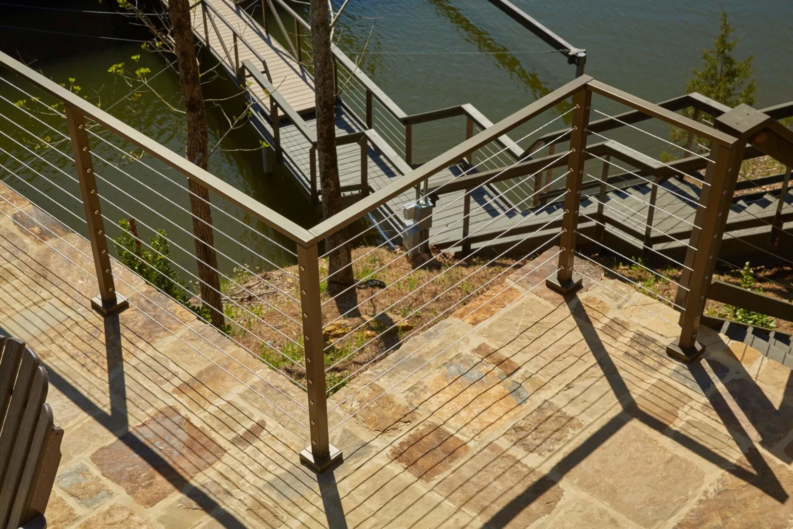 Looking down over bronze cable railing on a stone patio toward a dock below