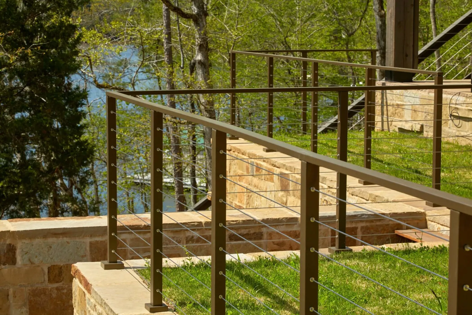 Bronze railing following stone steps and a retaining wall down toward the water