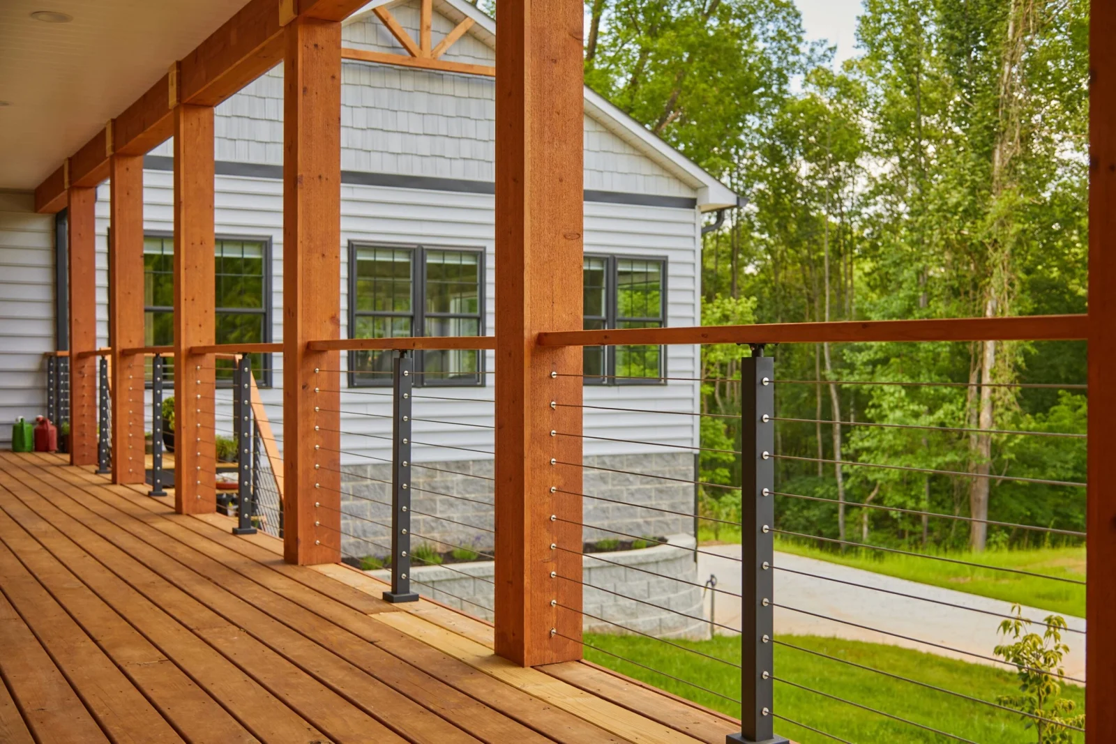 Porch decking with black cable posts running between timber columns toward the woods