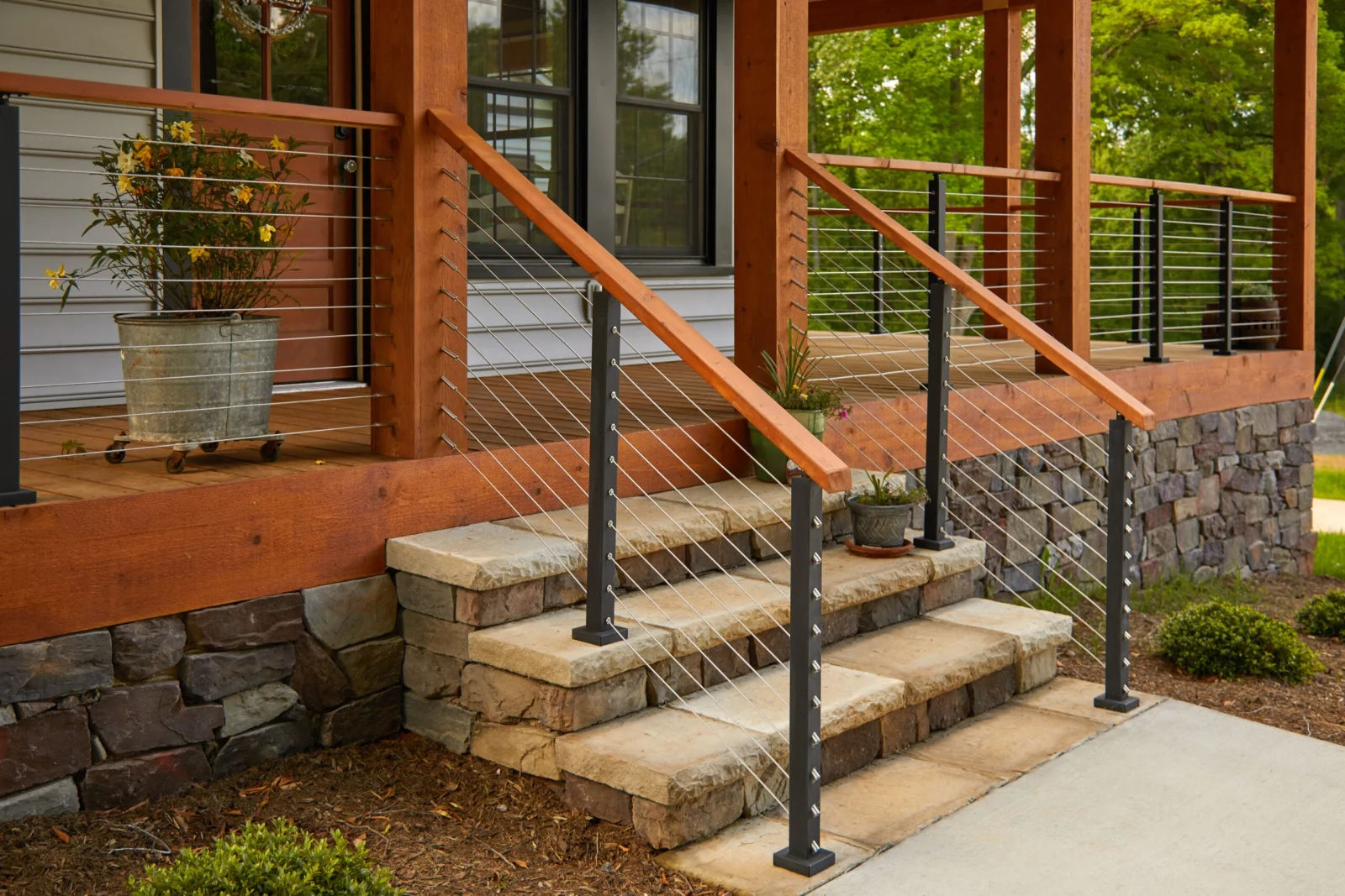 Stone steps rising to a porch behind cable railing on dark posts with wood caps