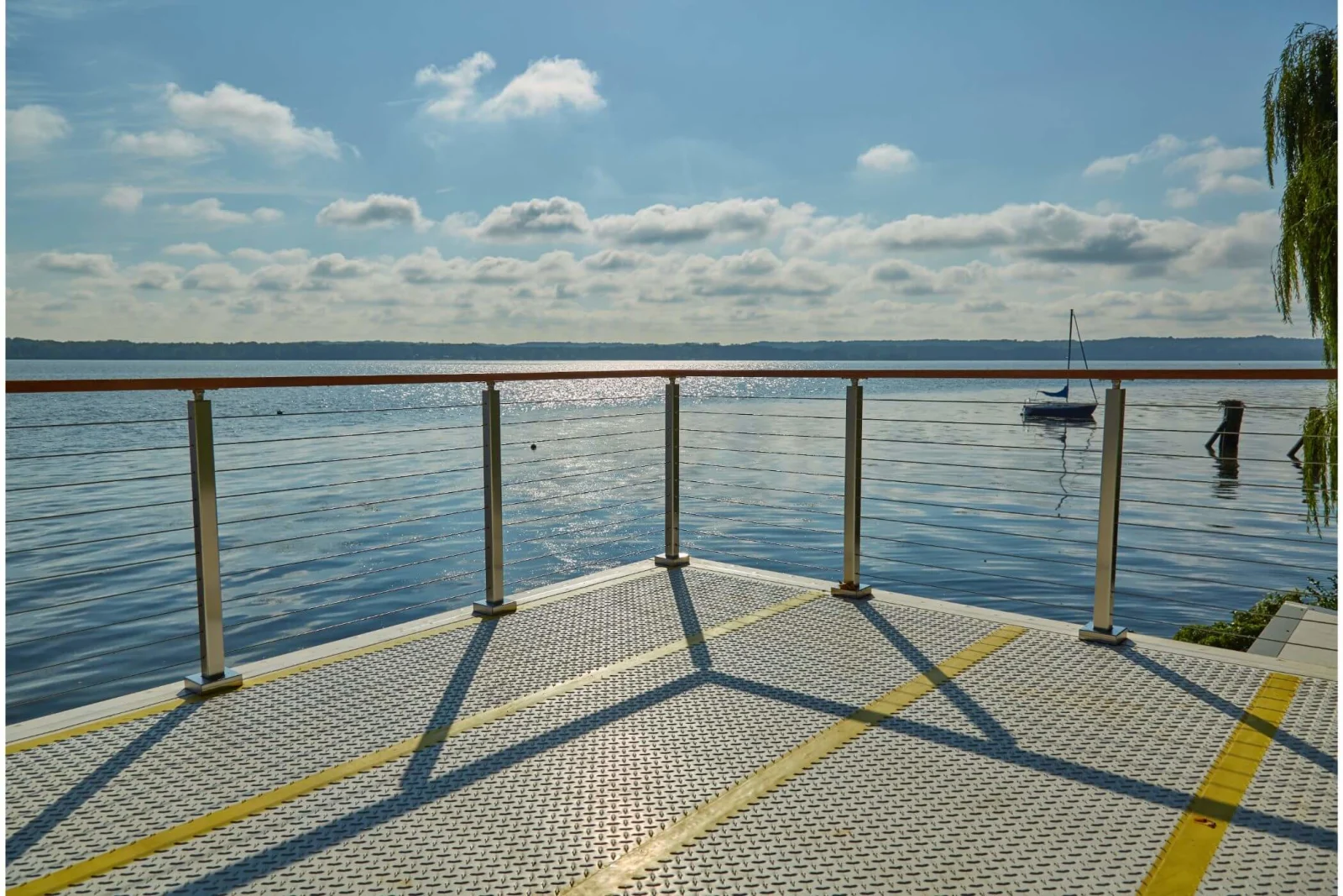 Grated pier decking and yellow stripes beneath a run of stainless cable railing