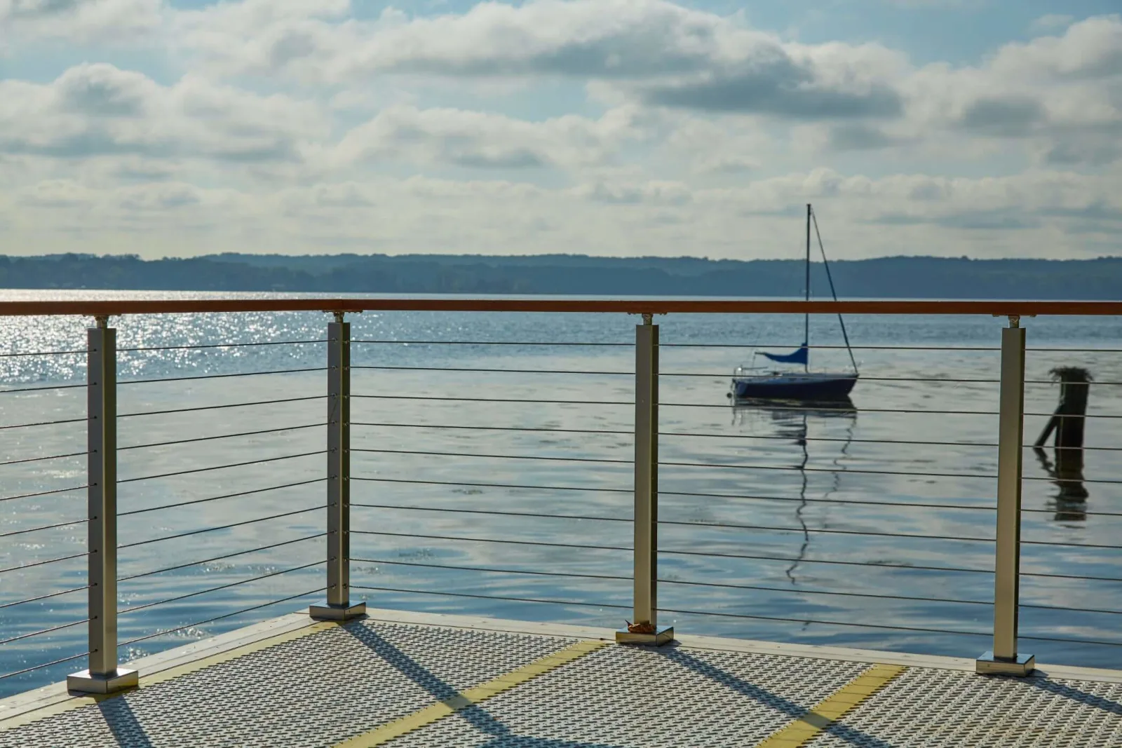 Sunlit open water past a grated dock edged in wood-capped cable railing