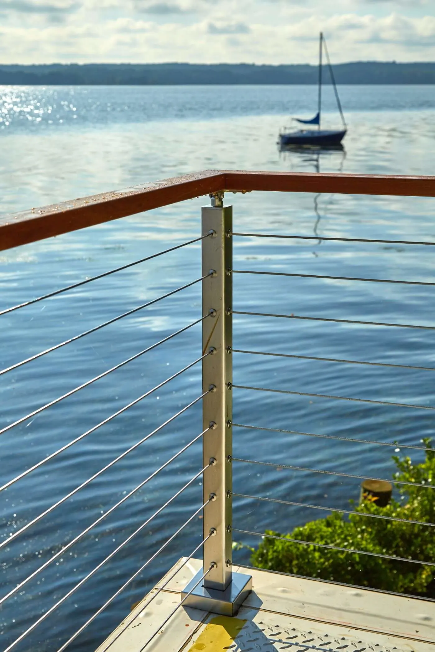 Rod railing at the end of a dock with a sailboat on the bay