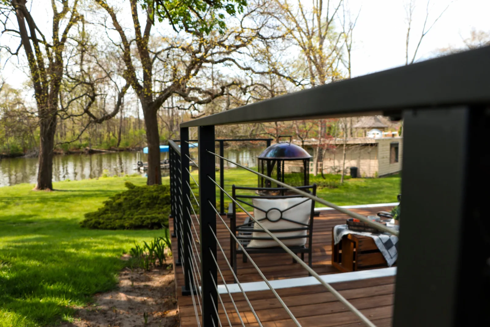 Black cable railing wrapping a deck of lounge chairs above a lawn and creek