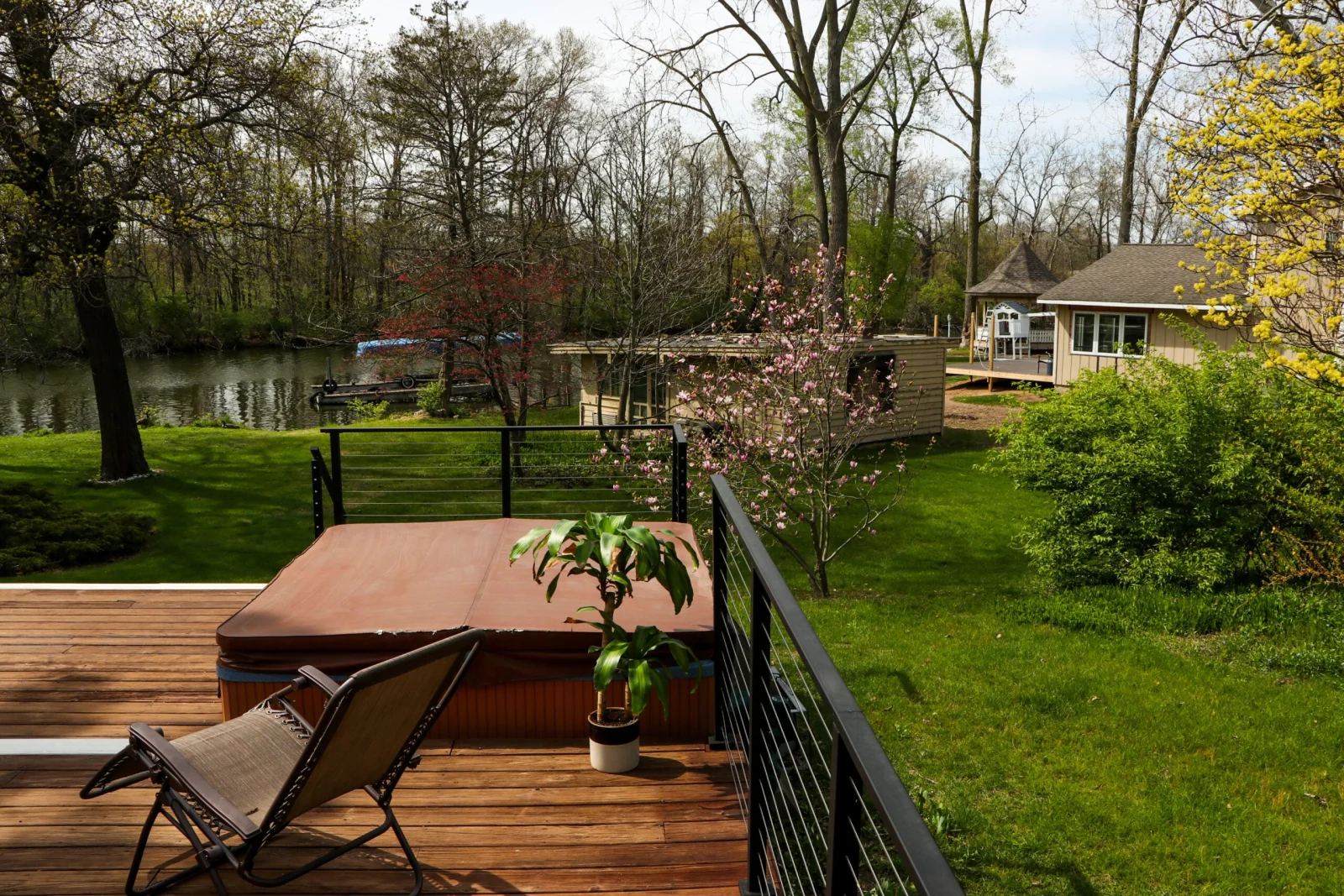 Backyard deck with a hot tub behind black cable railing overlooking a pond