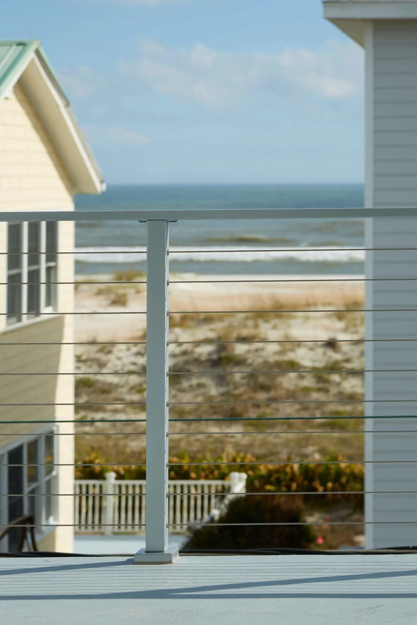 Gray flat-top cable post on a balcony with dunes and ocean beyond