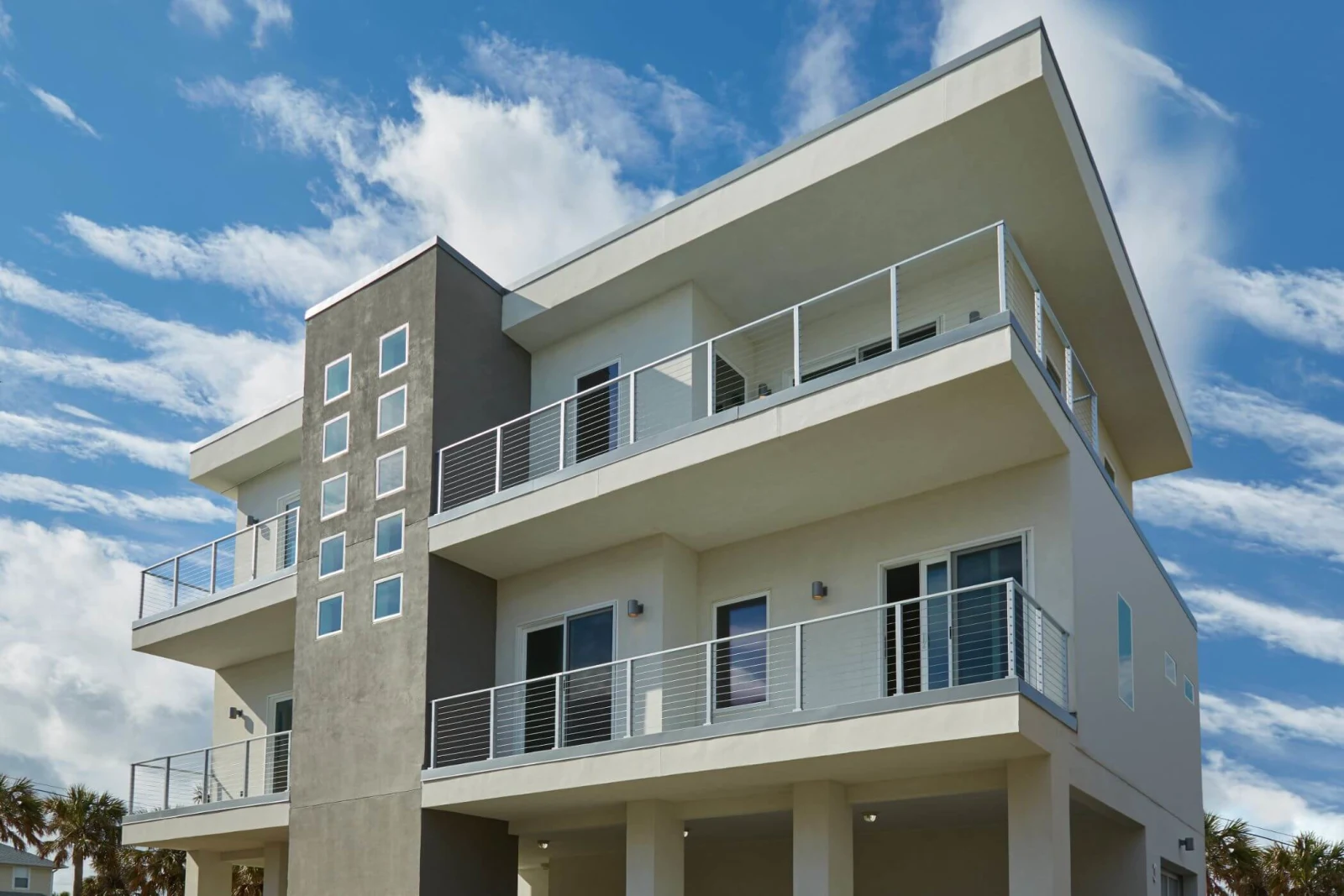 Three-story beachfront home with cable railing on stacked balconies against a blue sky