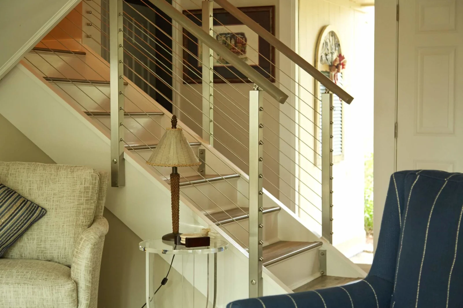 Straight stair run with cable infill viewed across upholstered chairs in the living room