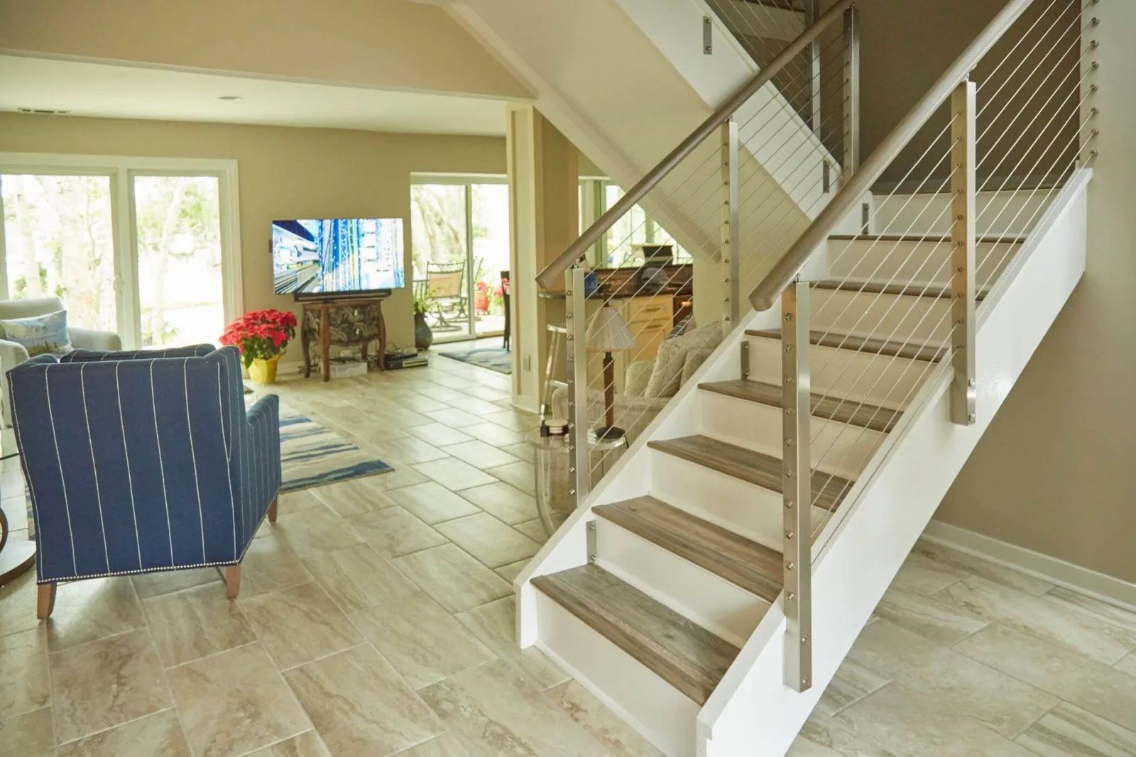 White-skirted stair with stainless cable railing rising from a tiled open living area