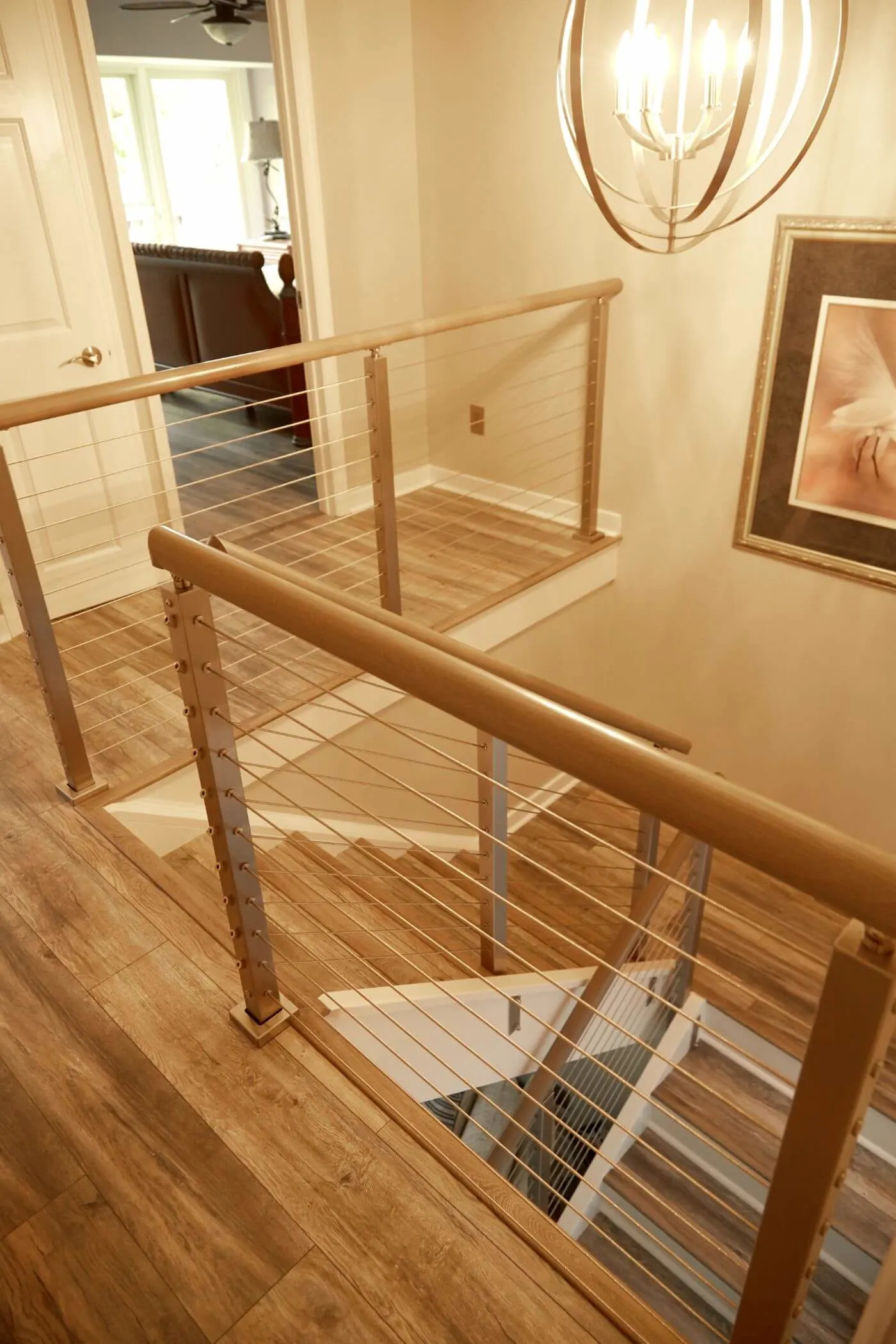 Upper hallway overlook with cable railing and wood handrail beneath a ring chandelier