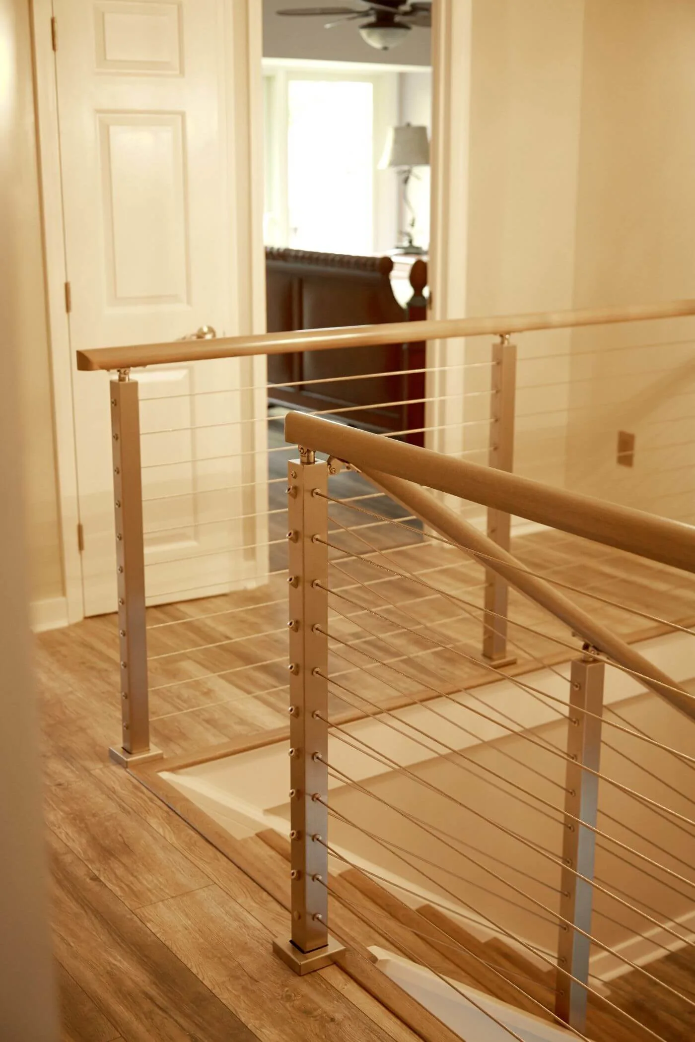 Upstairs landing railing with stainless posts meeting a wood handrail near a doorway