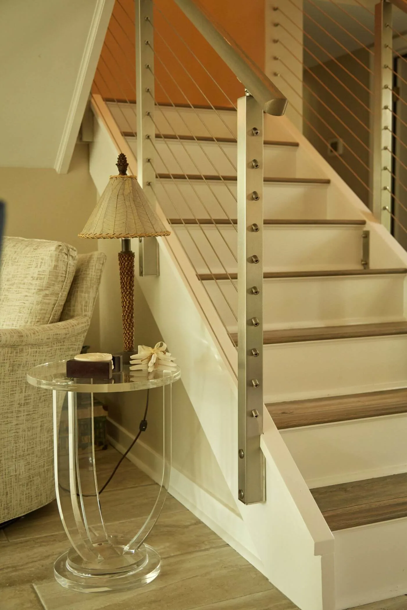 Interior stair with stainless posts and wood handrail beside a living room seating area