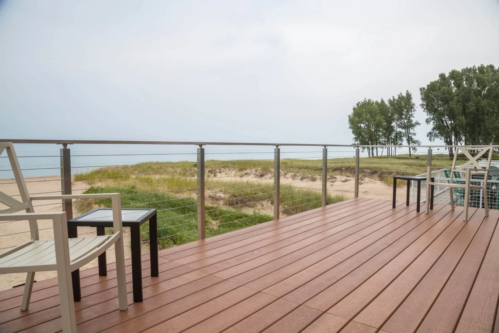 Stainless side-mount posts and cable edging a broad deck above dune grass and shoreline