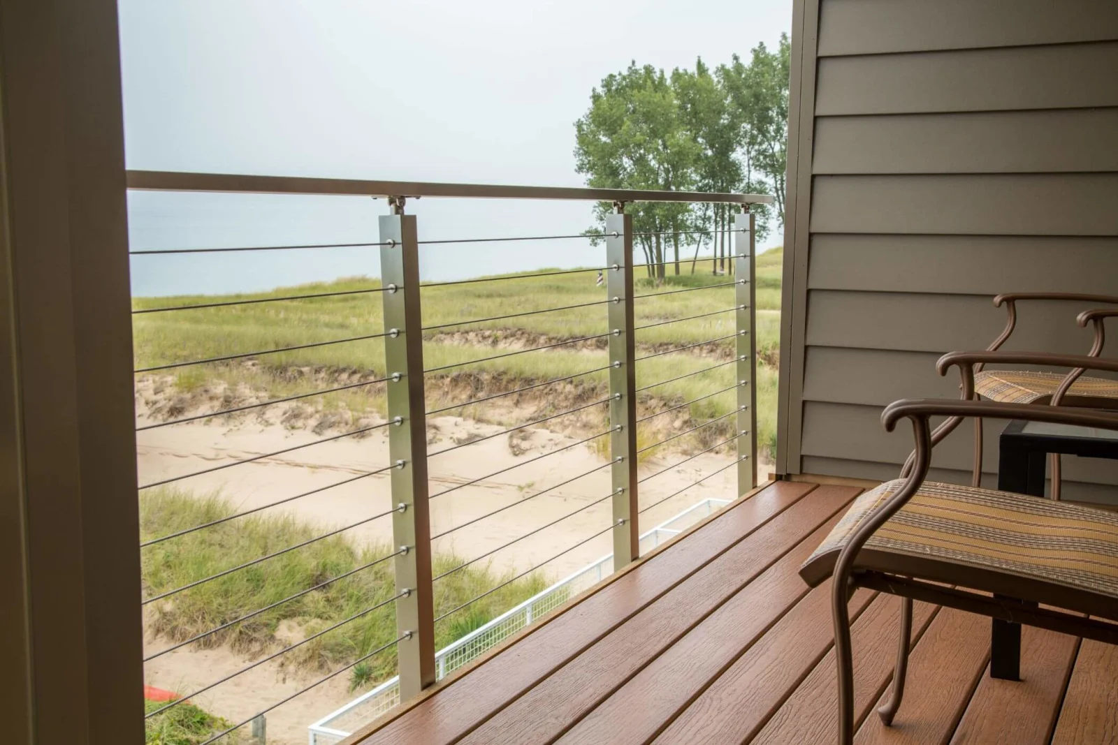 Covered balcony with cable railing looking over dune grass toward the shoreline