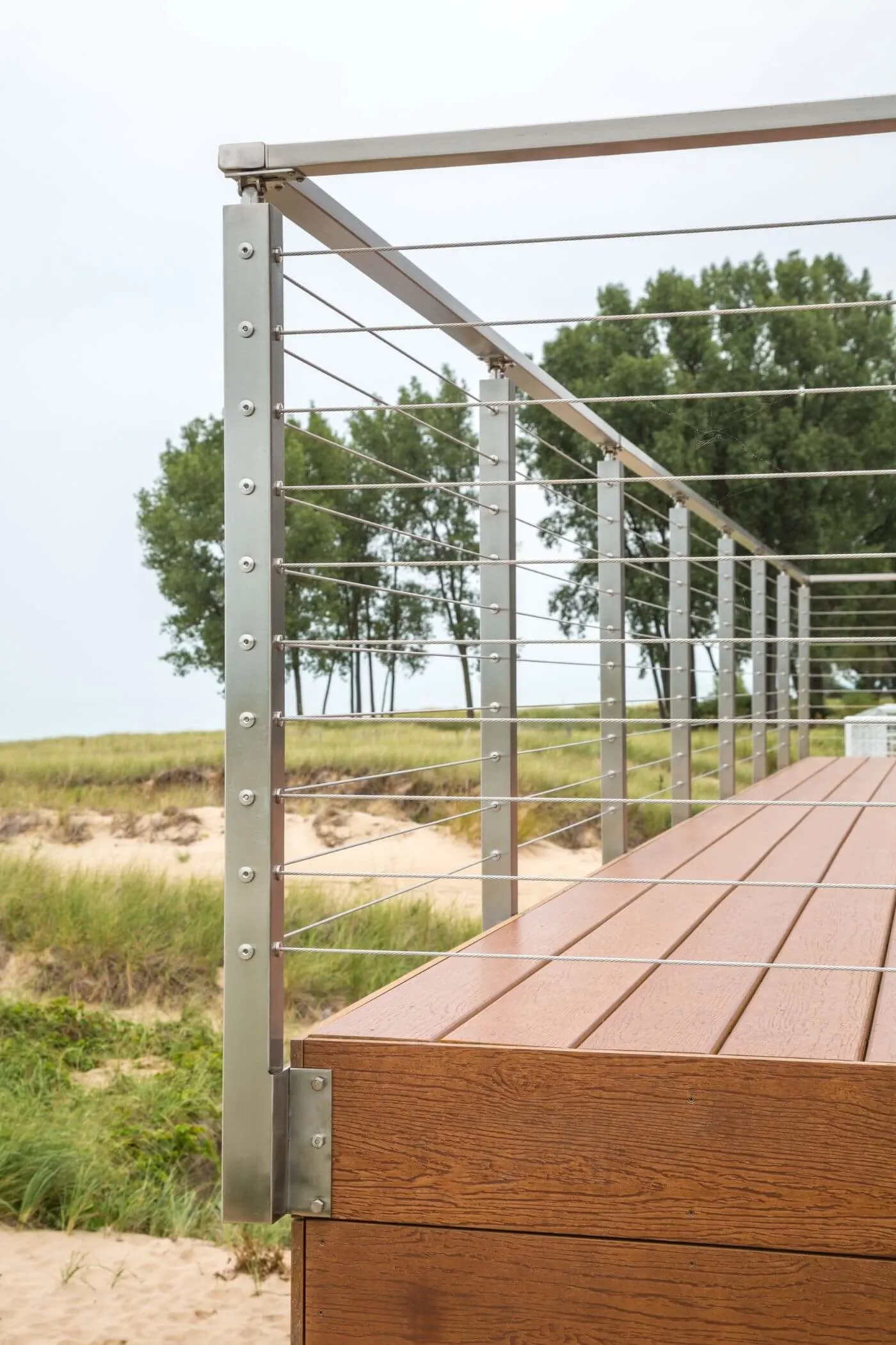 Side-mounted cable posts at a deck corner above the dune with trees behind