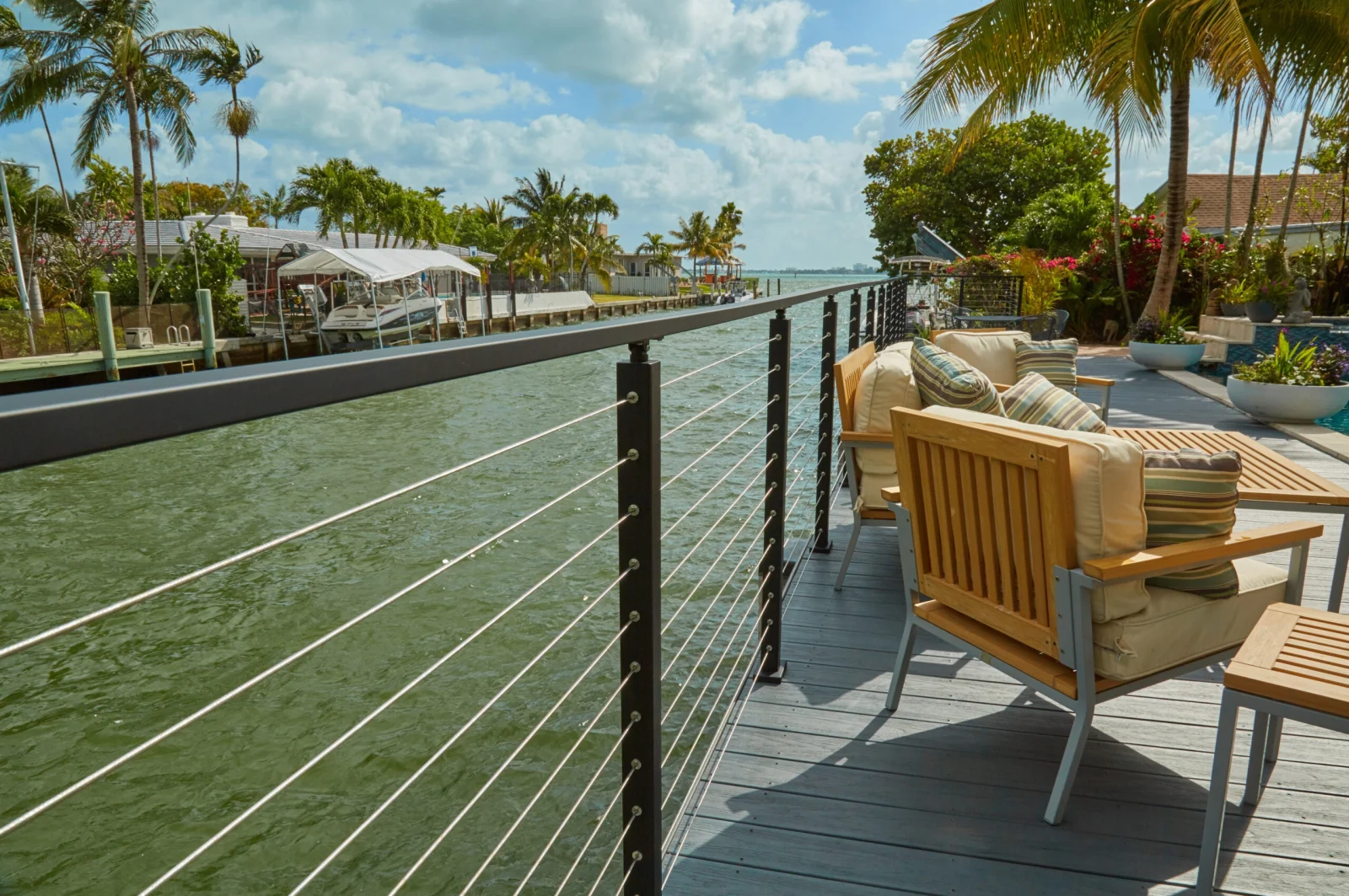 Black cable railing along a canal-side deck with slatted lounge seating under palms