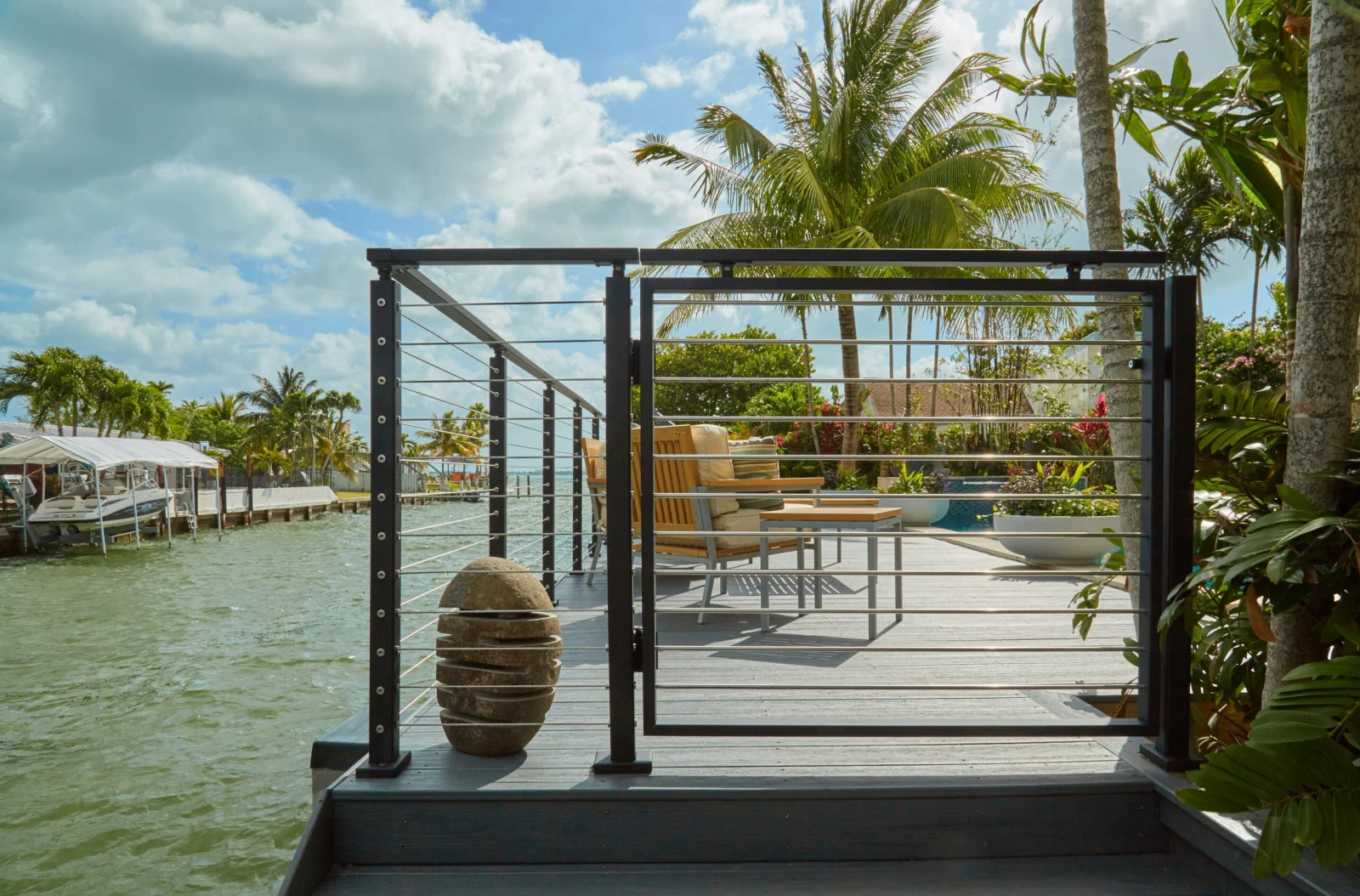 Open cable gate framing a palm-lined patio and seating area beyond the dock
