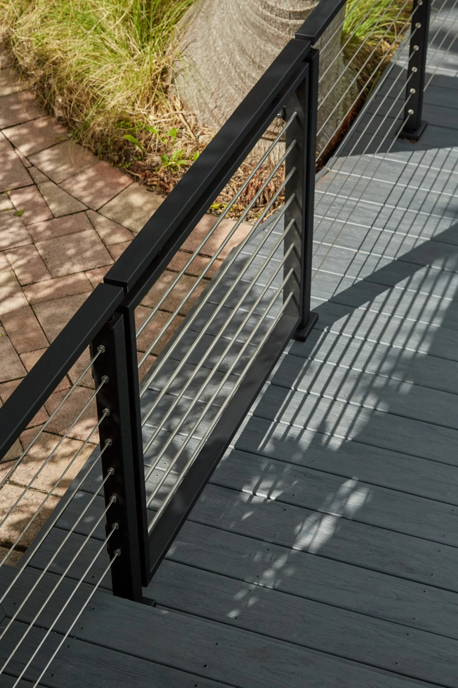 Black cable railing dividing gray decking from a brick paver path