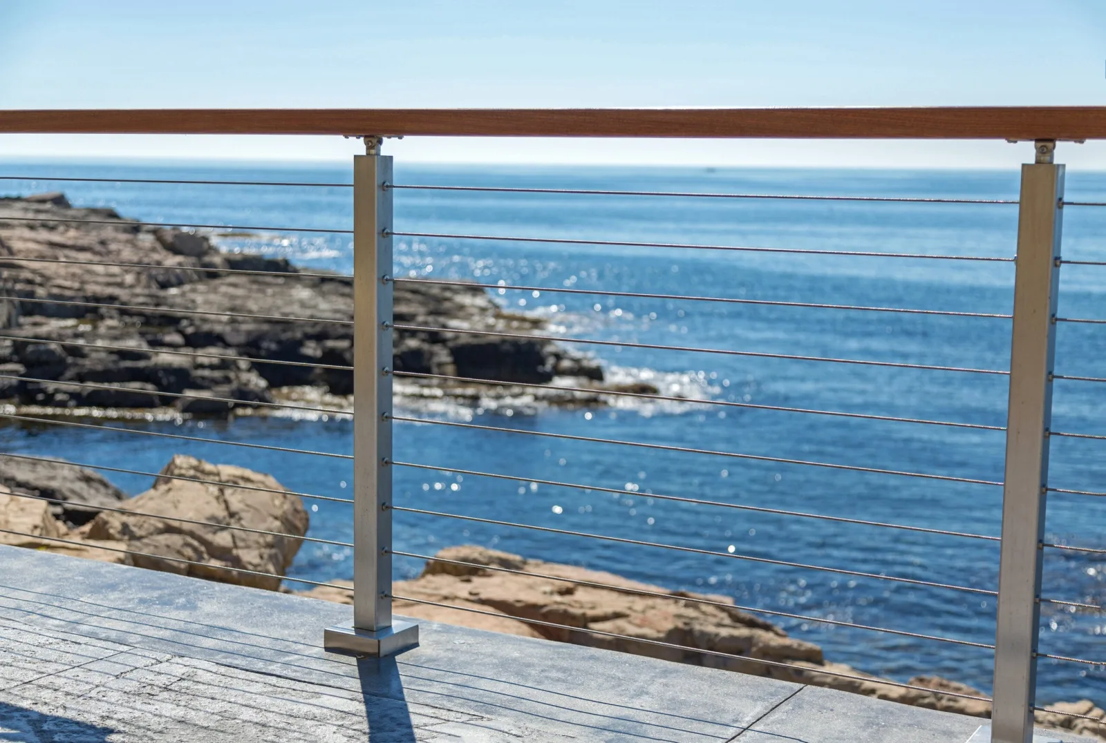Cable railing with wood top rail overlooking sunlit water and ledge rock