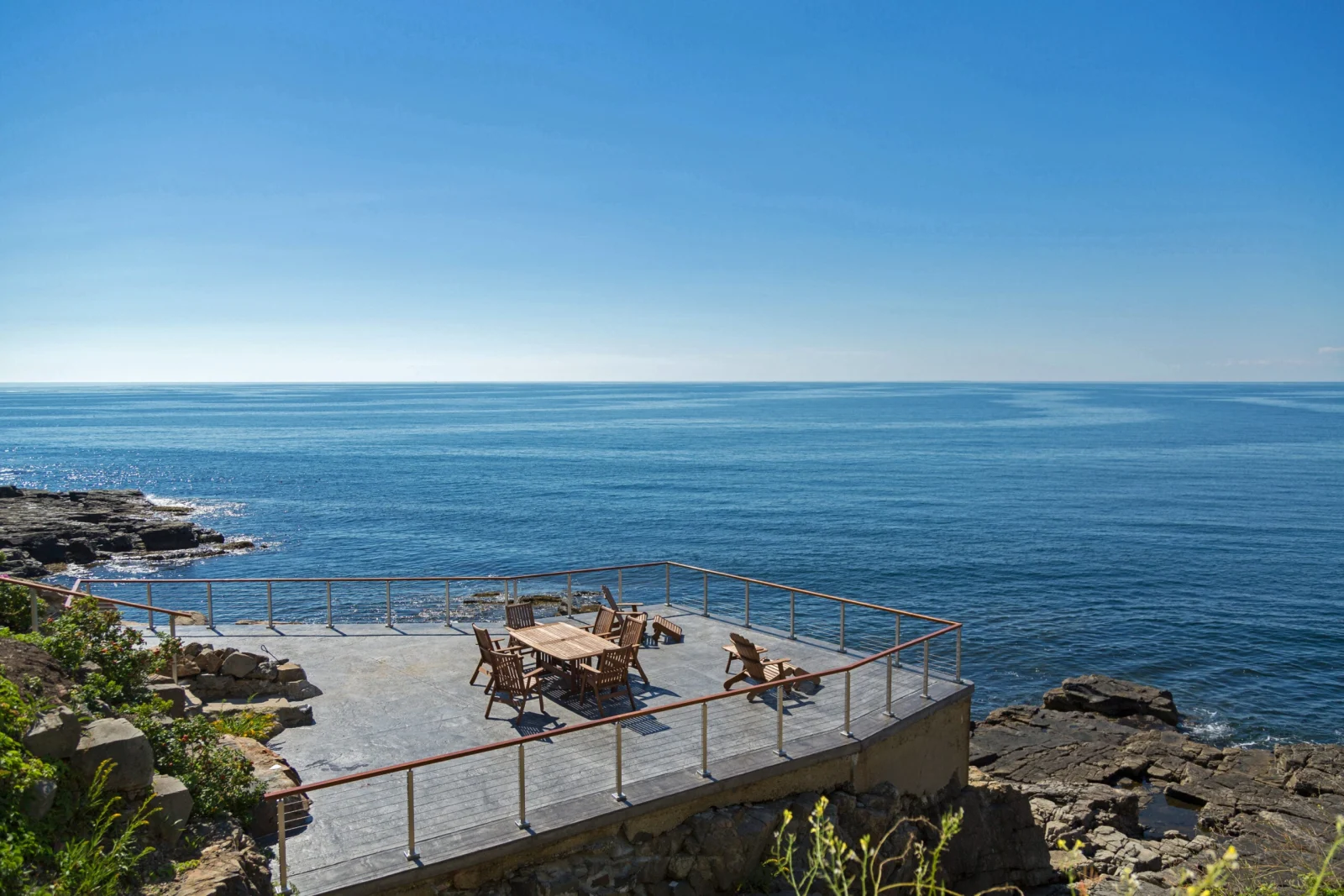 Rocky coastal bluff terrace with slim perimeter railing, patio table, and open ocean