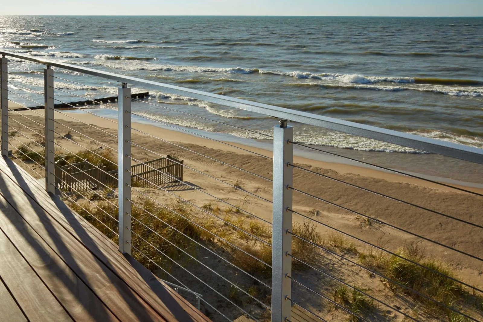 Long run of silver cable railing casting shadows across a lakefront deck