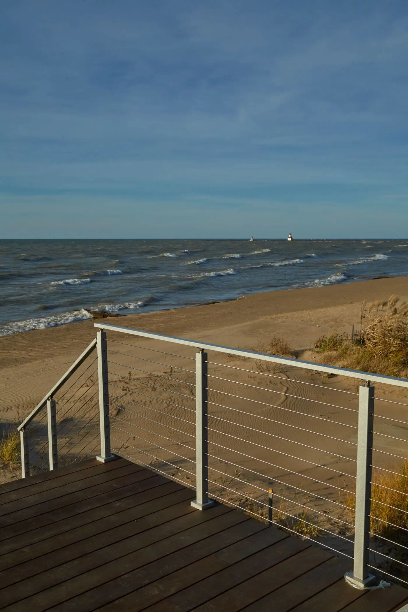 White posts and taut cables framing a sand beach from a wood deck