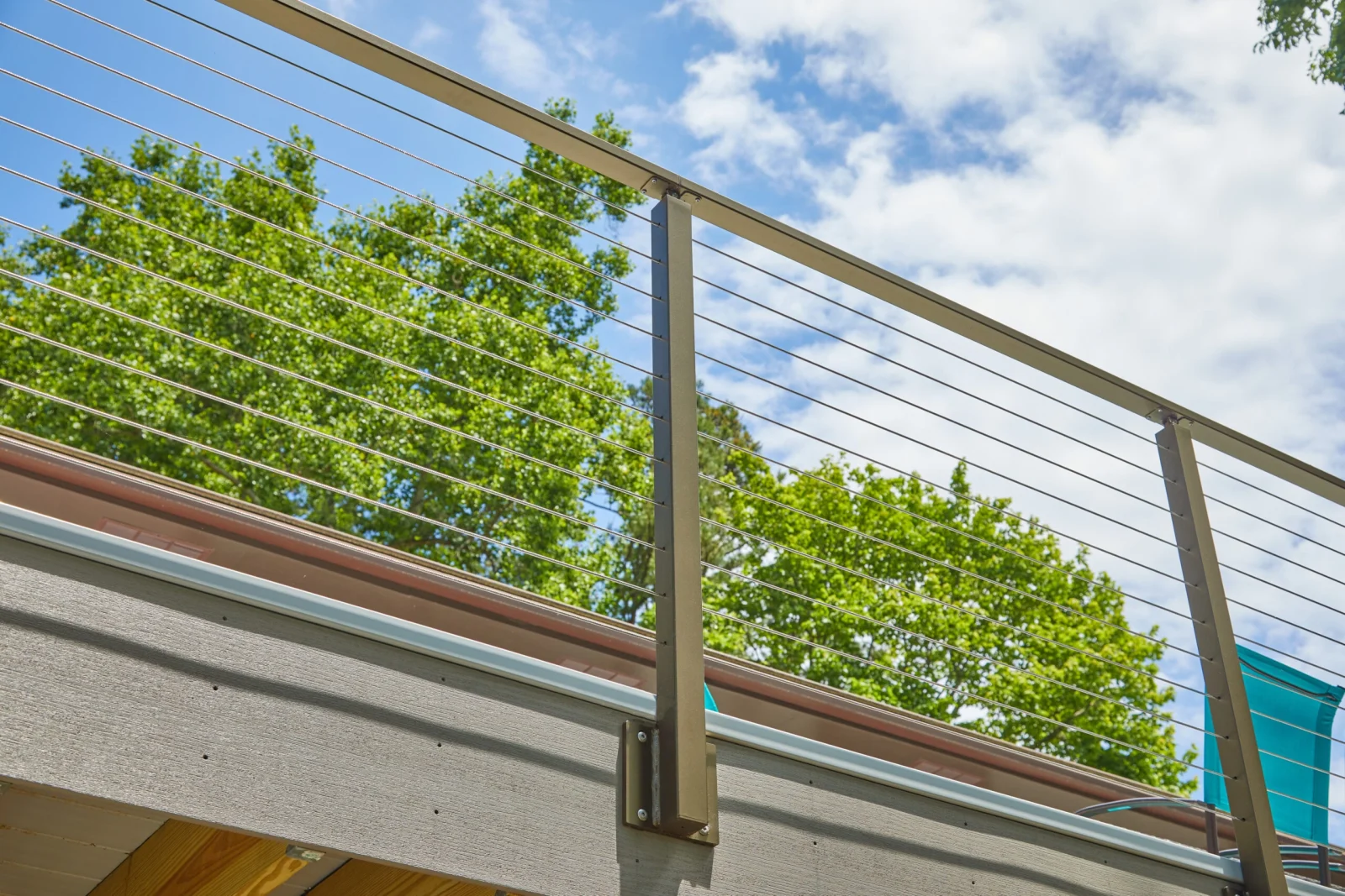 Upward view of bronze-topped posts and horizontal cables against sky and treetops