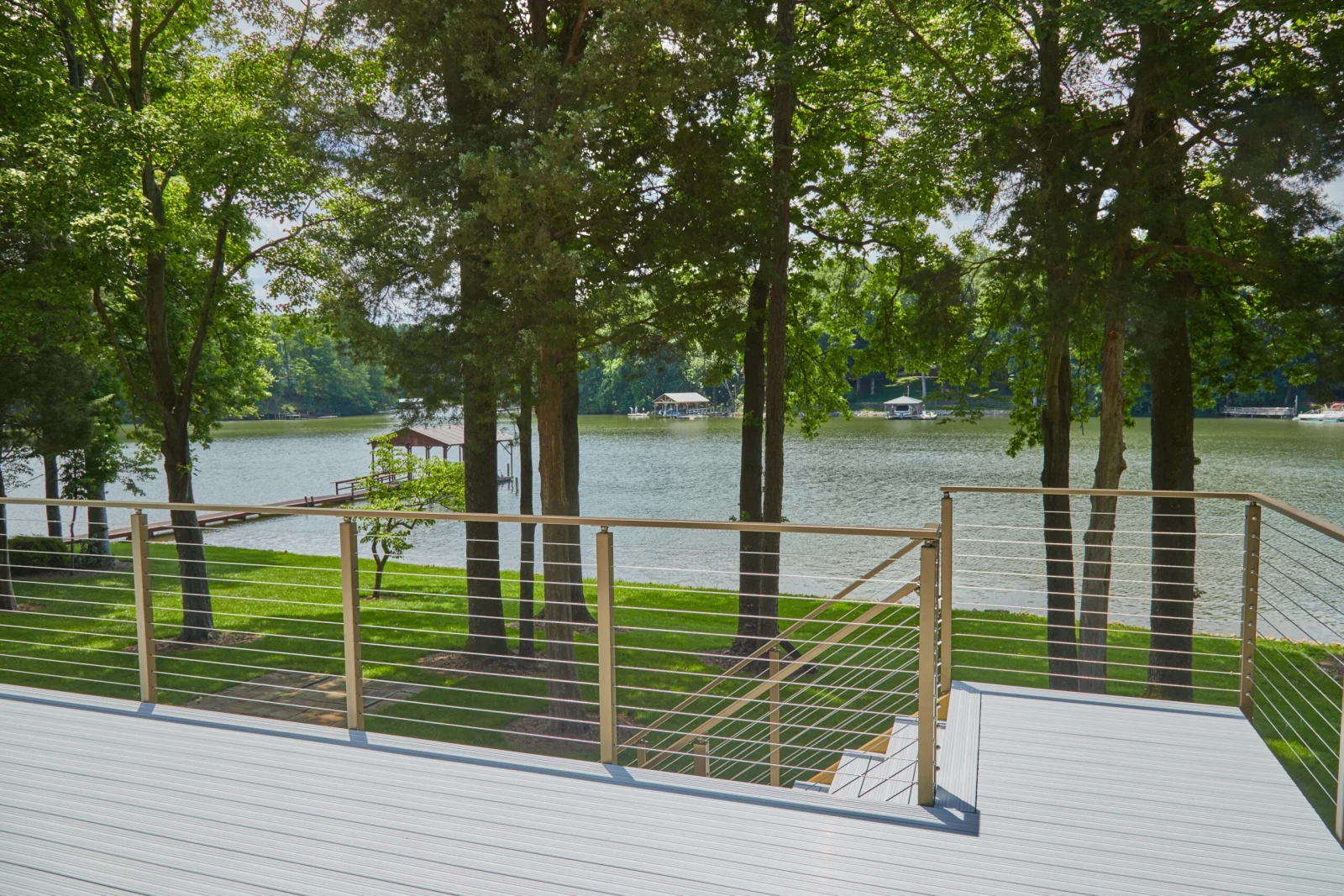 Cable railing on tan posts edging a deck among tall trunks above a lake
