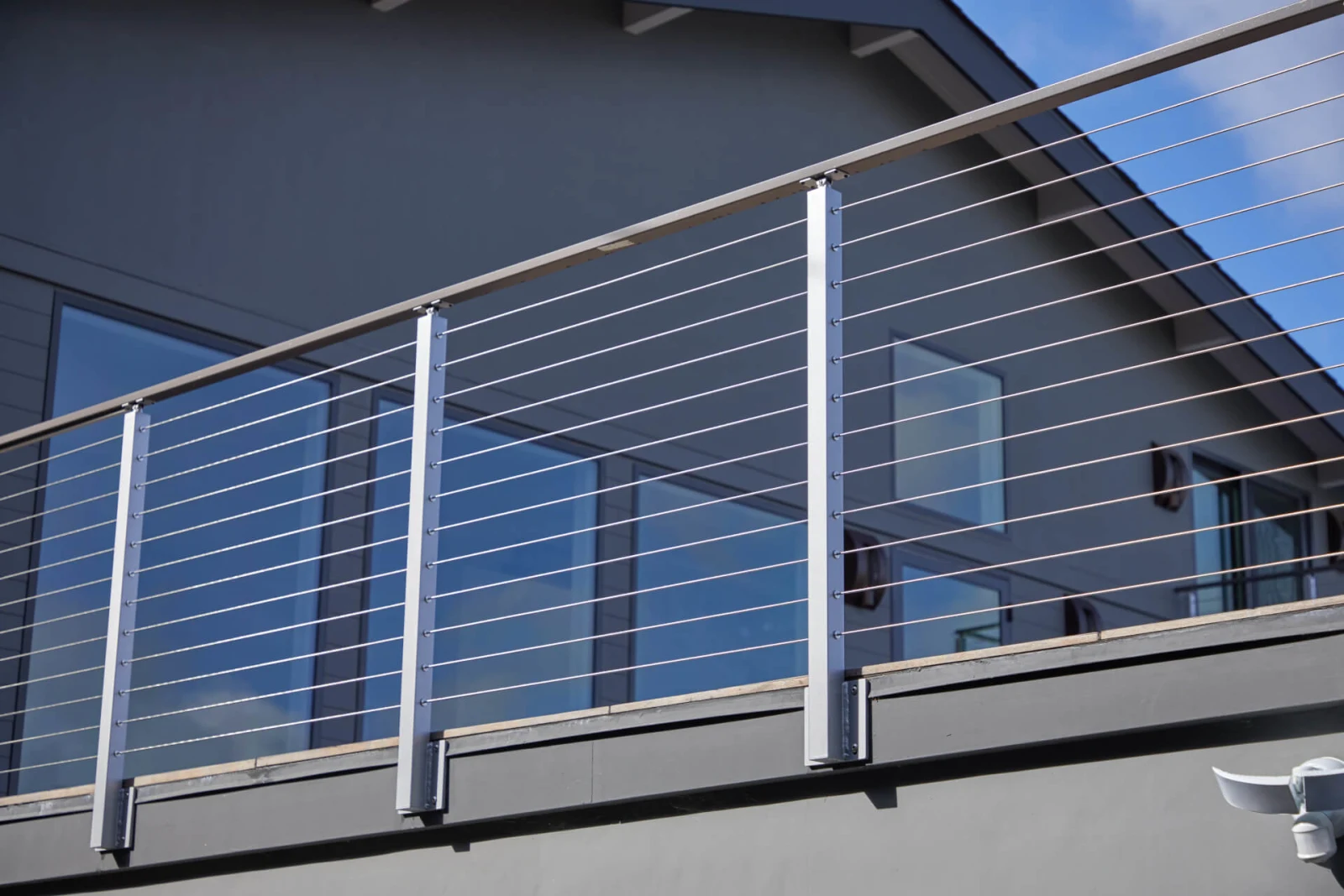 Balcony run mounted to gray siding, cables catching light beside tall windows