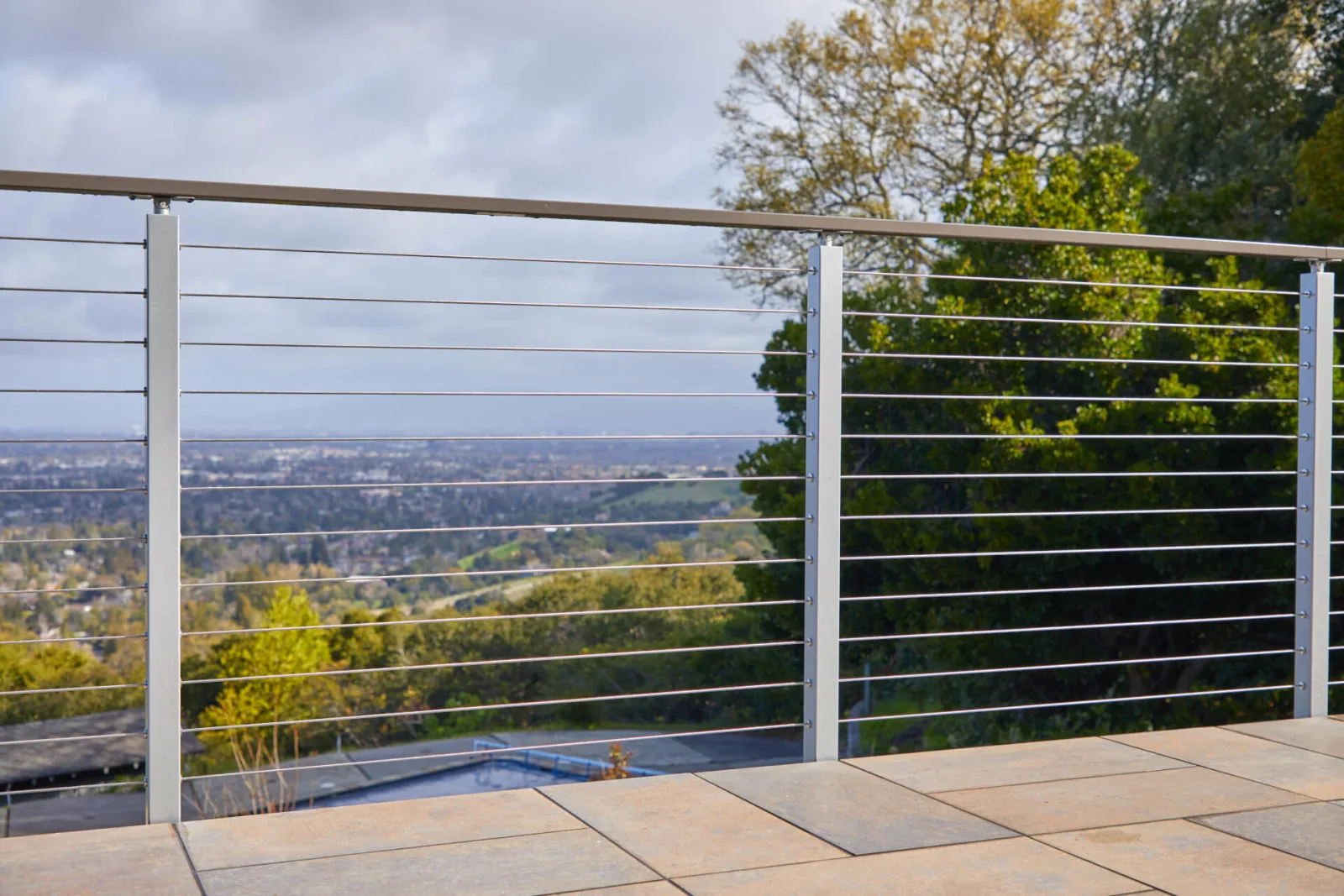 Tile terrace edged in cable railing under a cloudy valley sky