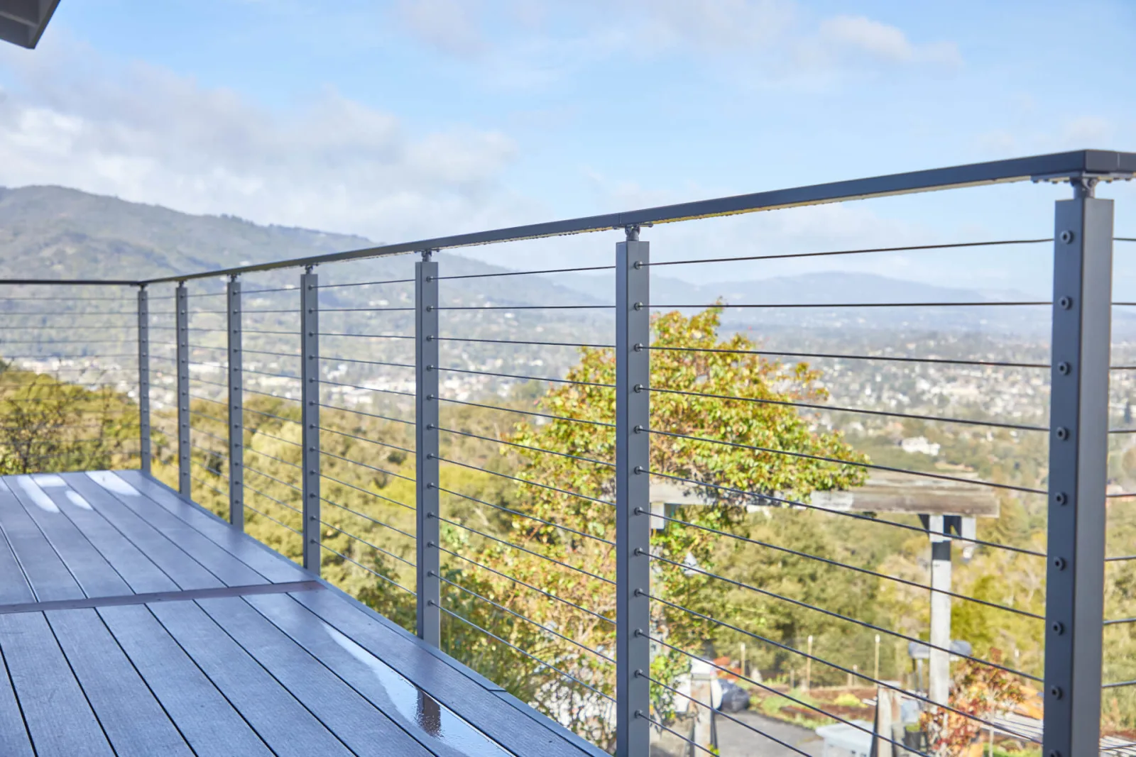 Silver posts and a gray top rail carrying cables along a deck above a wooded valley
