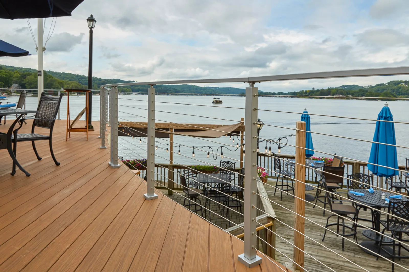 Cable railing curving around a restaurant deck of umbrella tables beside a lake