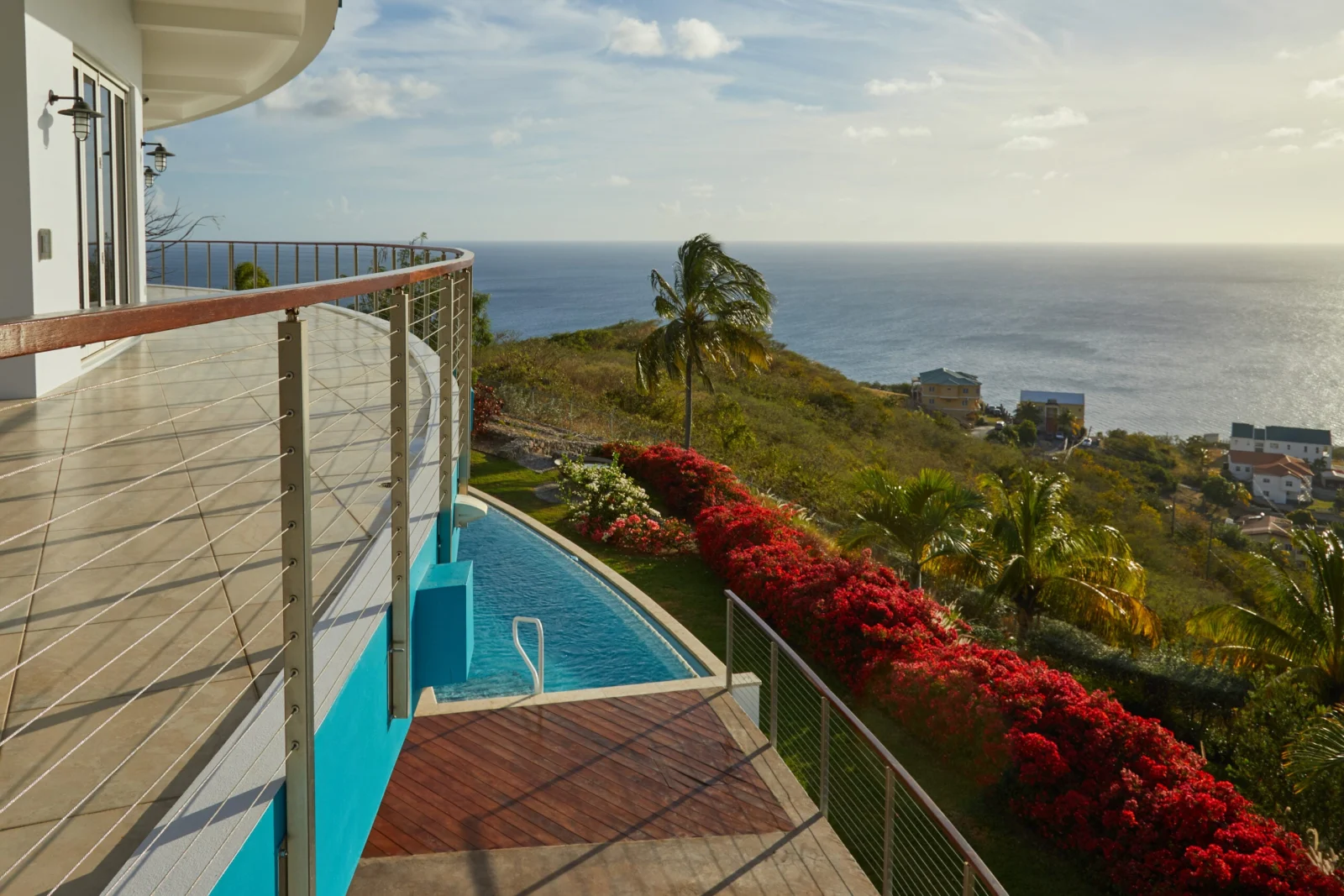 Tiled pool terrace edged with cable railing above red bougainvillea and open sea