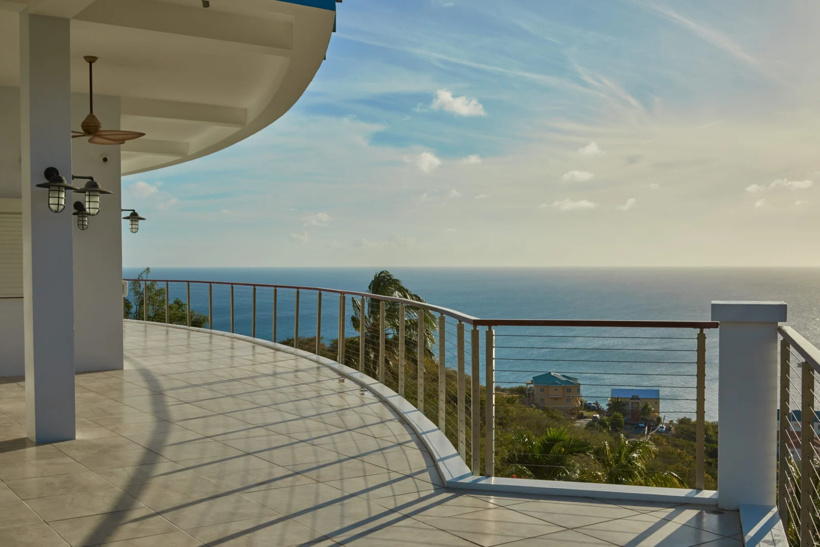 Curved balcony railing on a tiled terrace with ceiling fans and ocean beyond