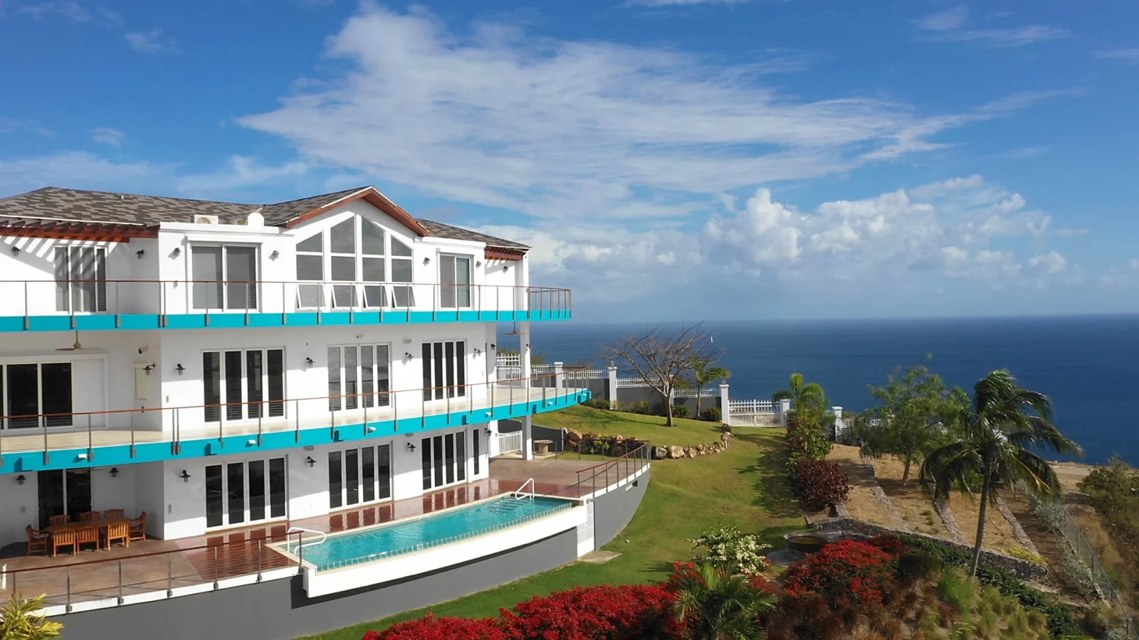 Three-story white house with railed balconies, a pool and open ocean