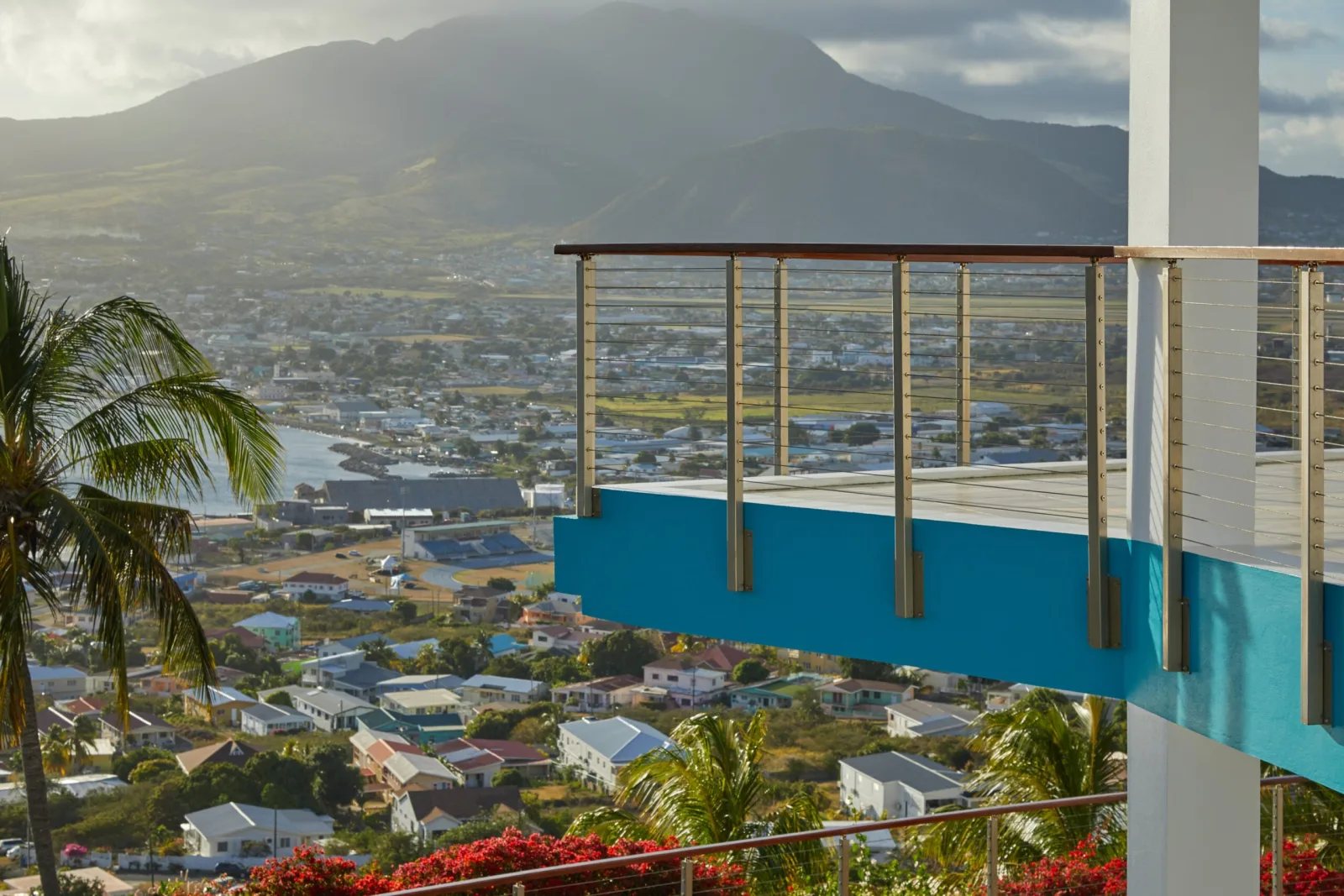 Cable railing above a turquoise balcony wall with mountain and town below