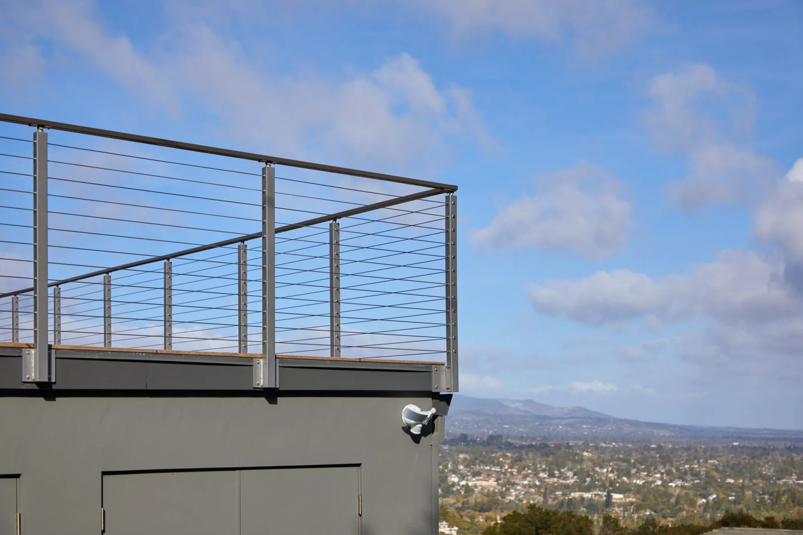 Rooftop railing outlined against clouds above a stucco wall and floodlight
