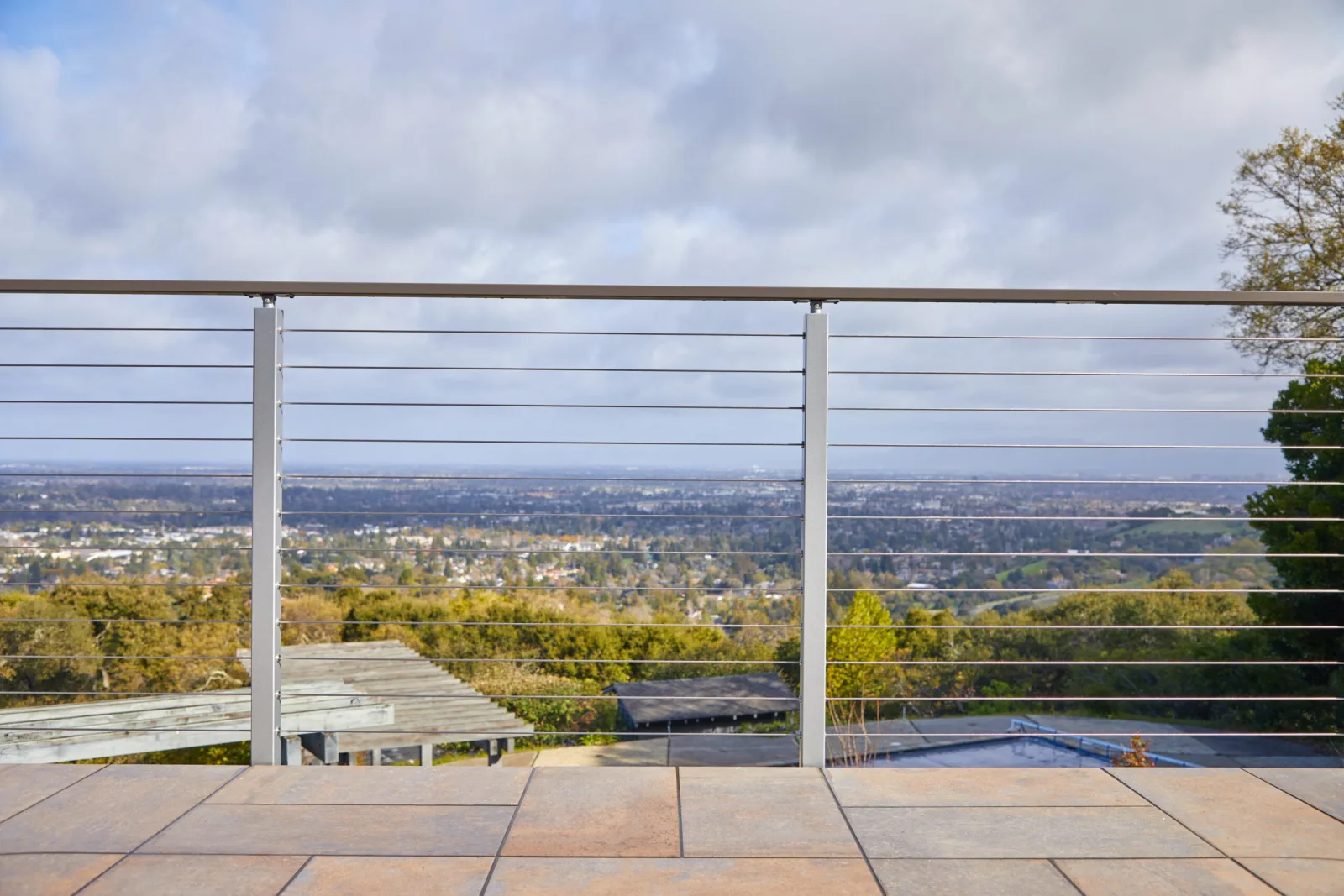 Cable railing across a stone patio opening to a wide valley under cloudy sky