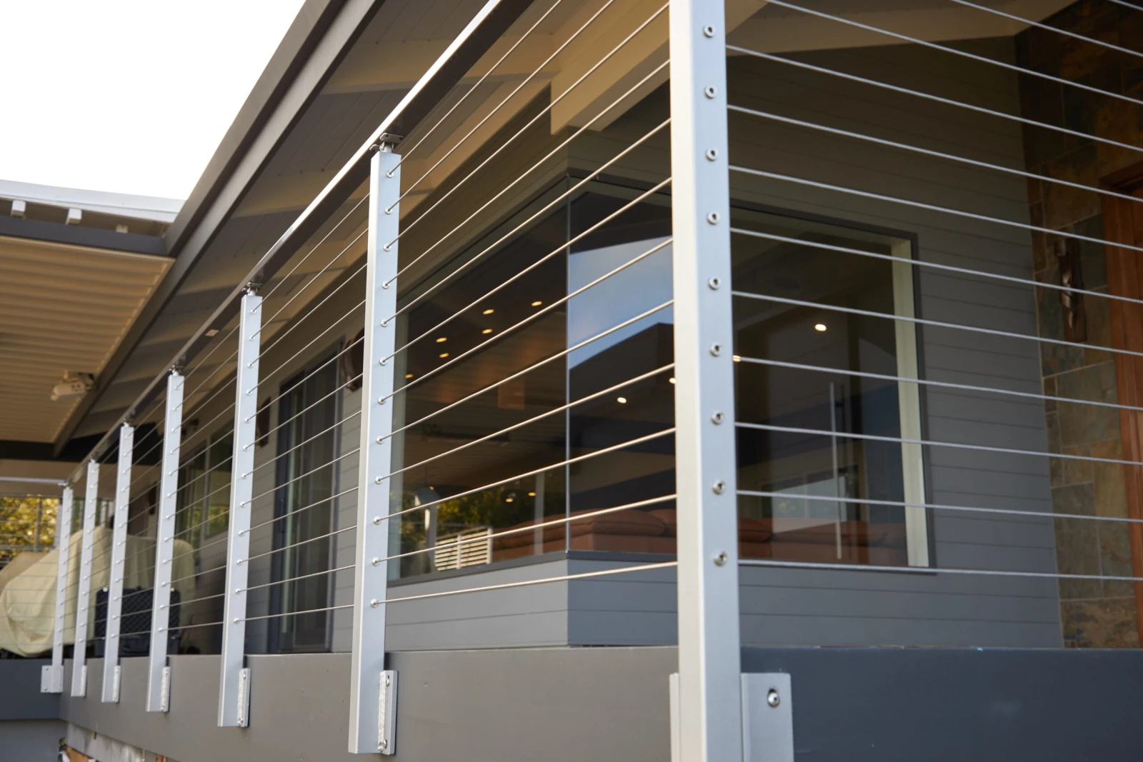 Slim posts and taut cables lining a covered walkway beside glazed walls