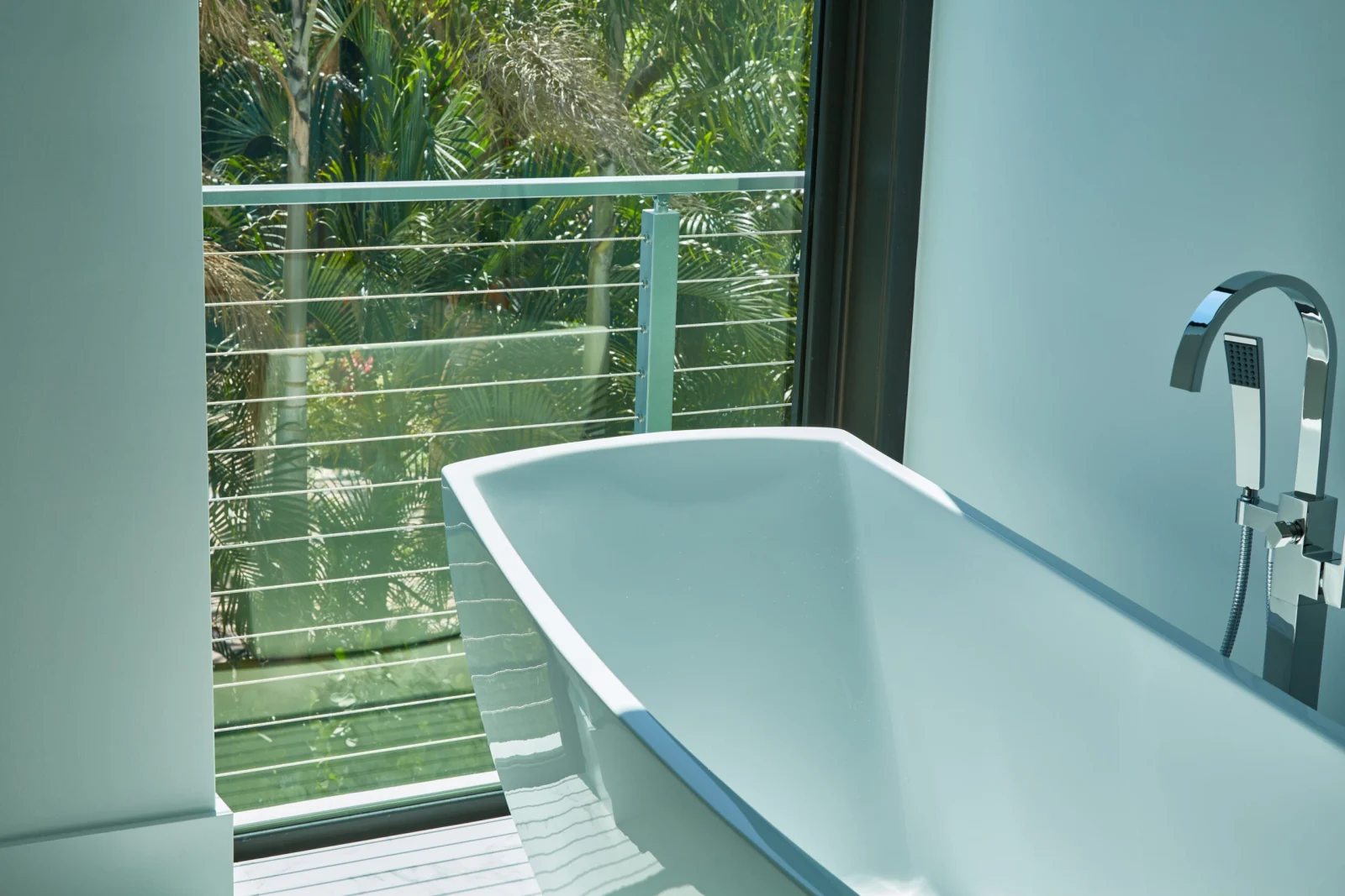 Freestanding tub beside glass doors opening onto a cable-railed balcony