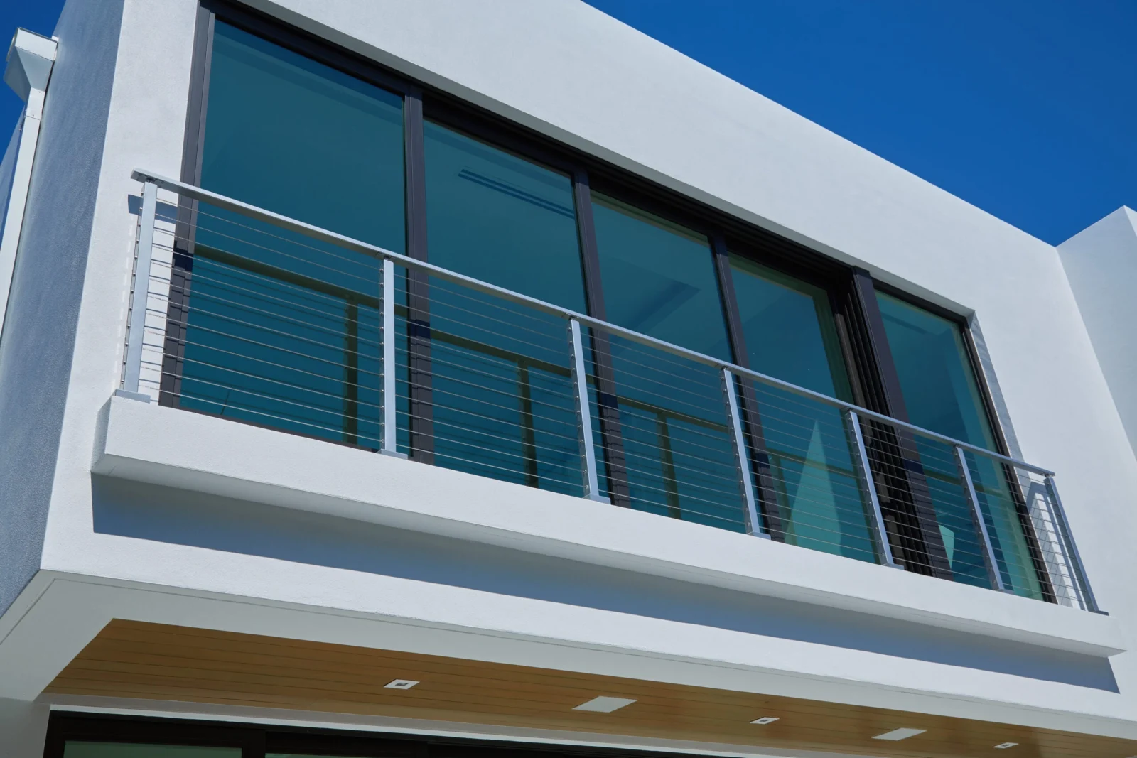 Juliet balcony with cable railing on a white stucco wall under deep blue sky