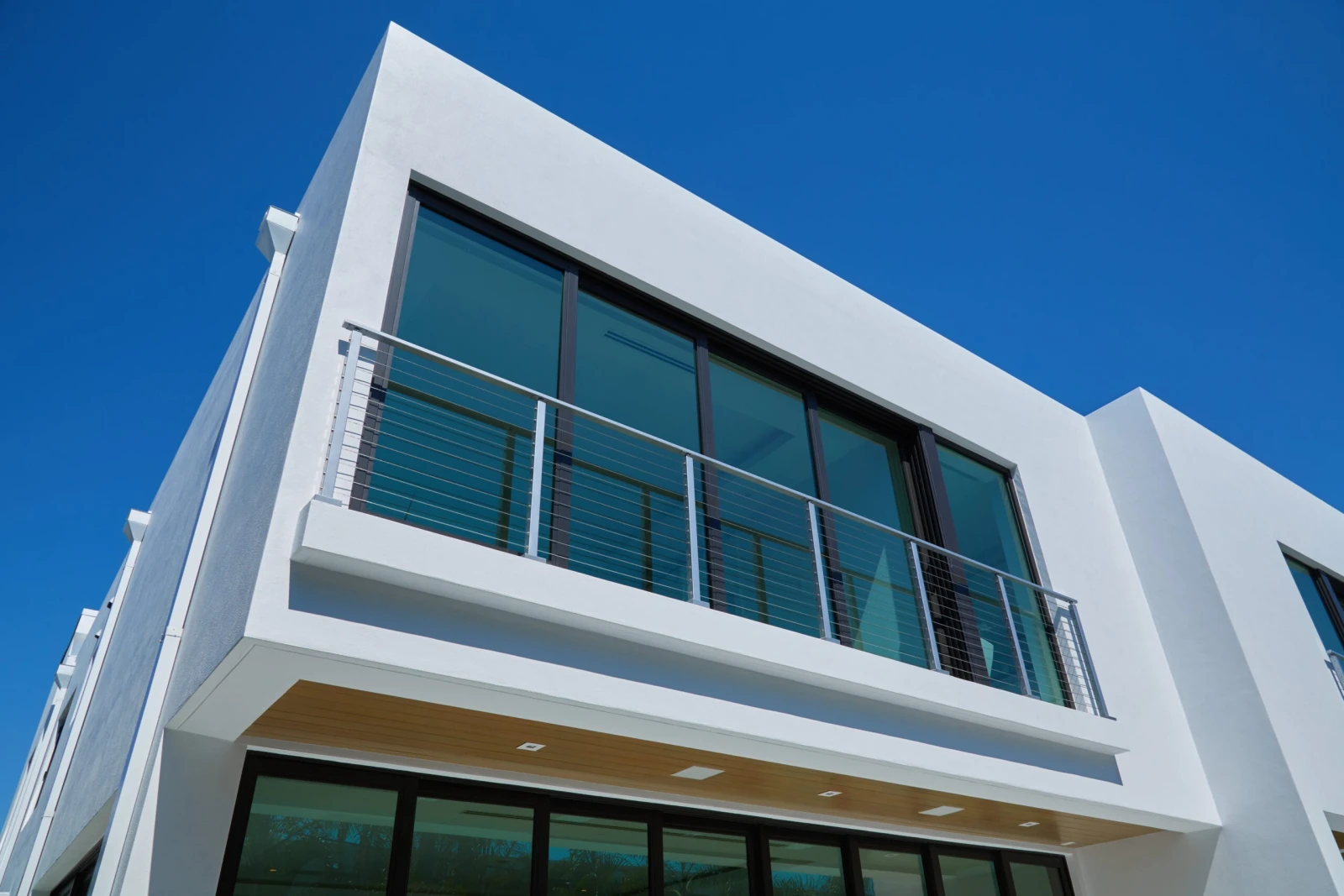 Corner of a white home with a narrow railed balcony against blue sky