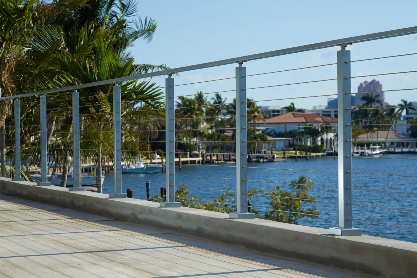 Shaded path with cable railing opening to palms and a sunny waterway