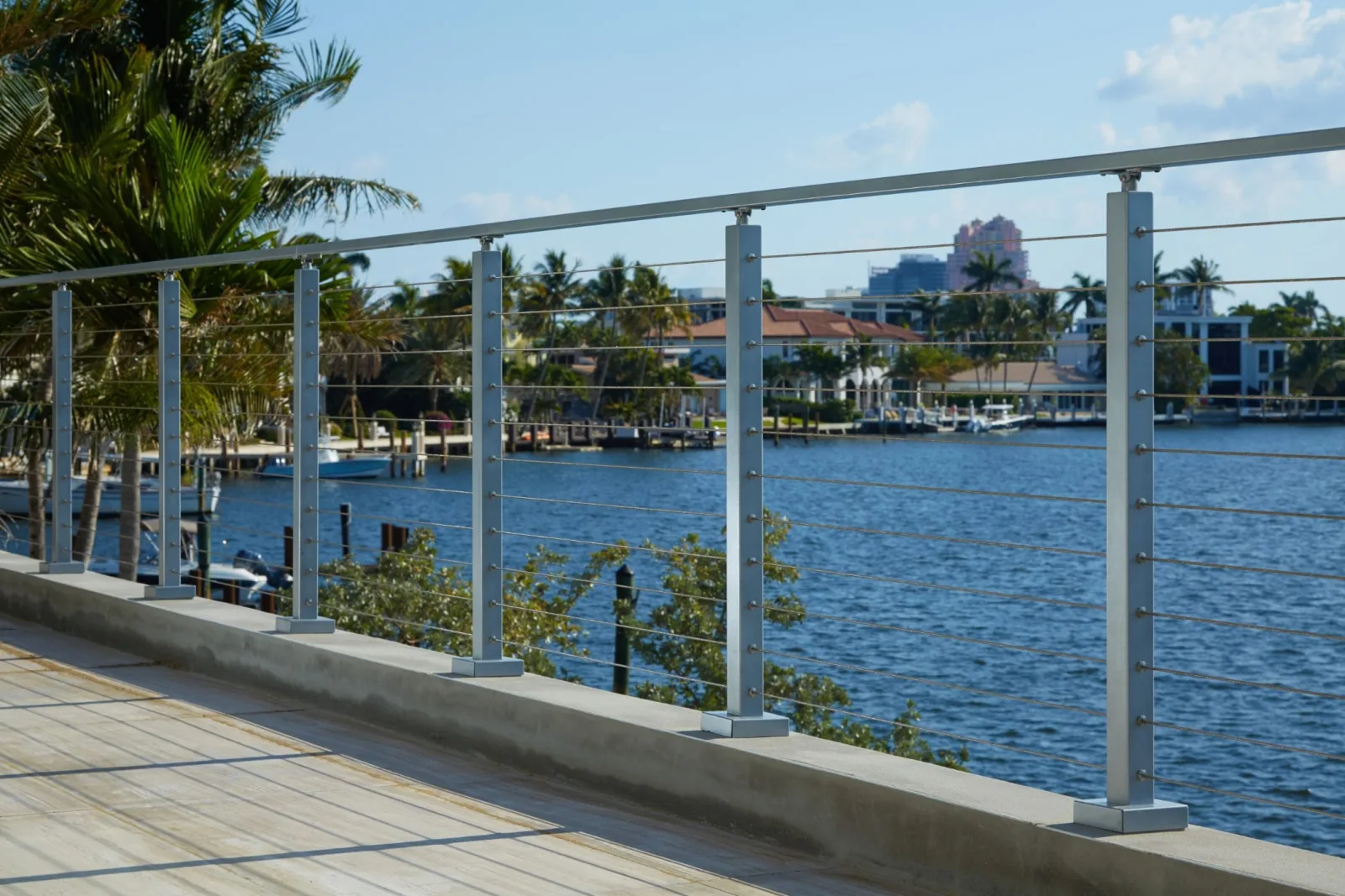 Railing following a curved concrete walkway past palms and waterfront homes